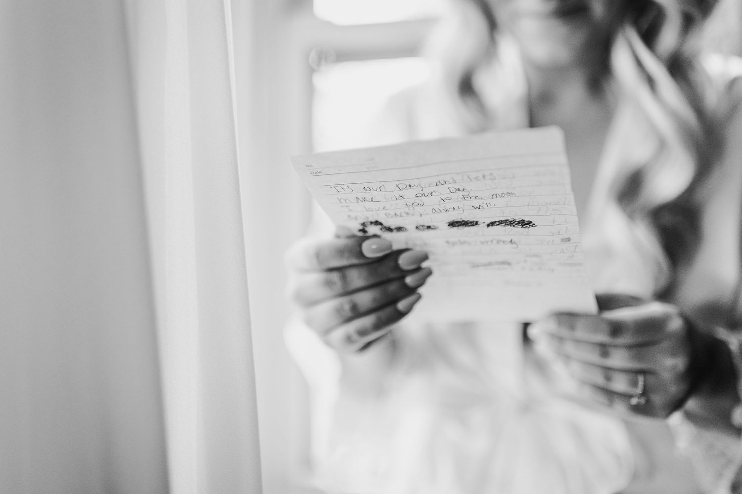 Bride reads a handwritten letter in black and white wedding photo.