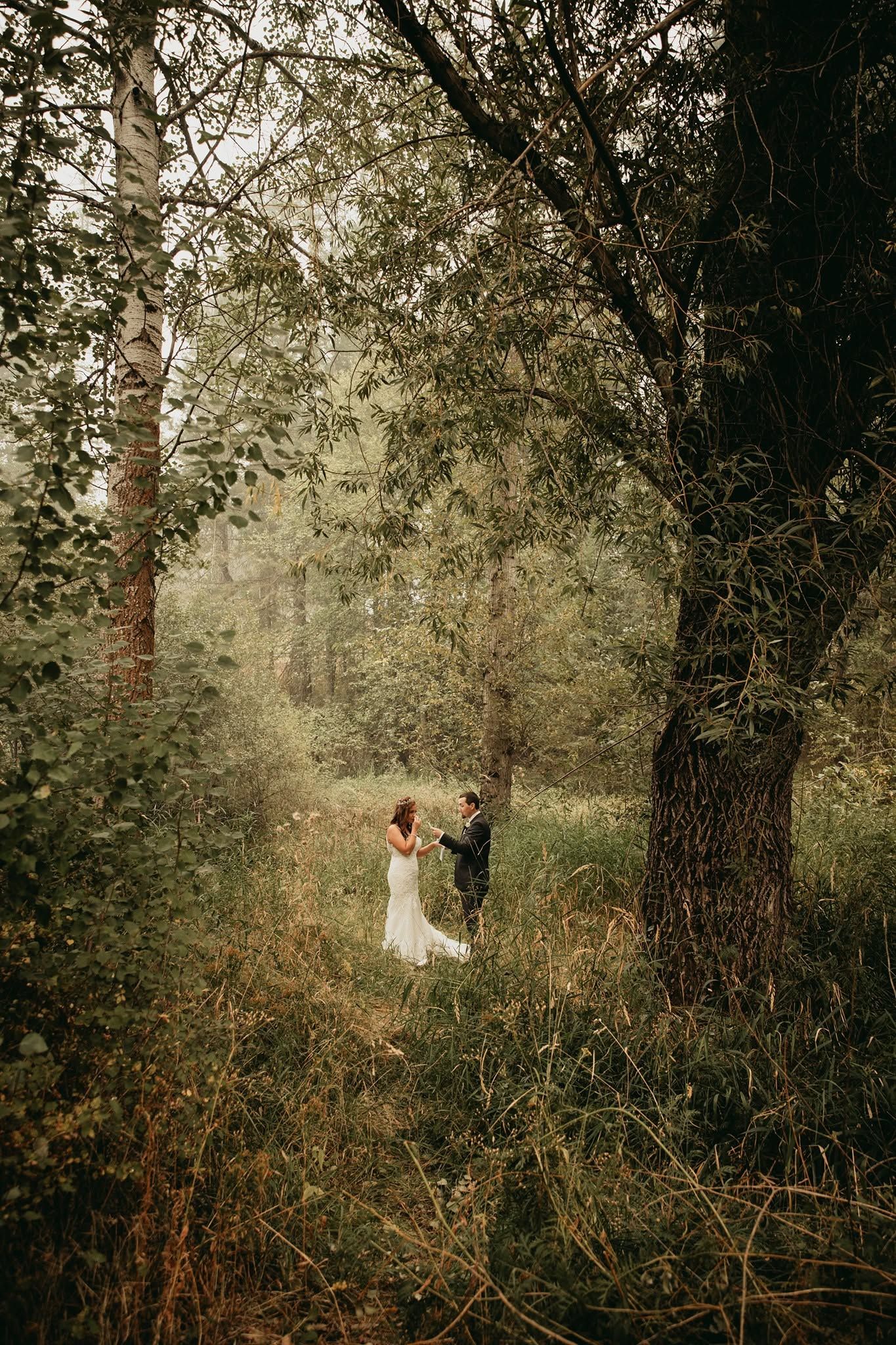 Bride and groom holding hands in a lush green forest during wedding portraits.