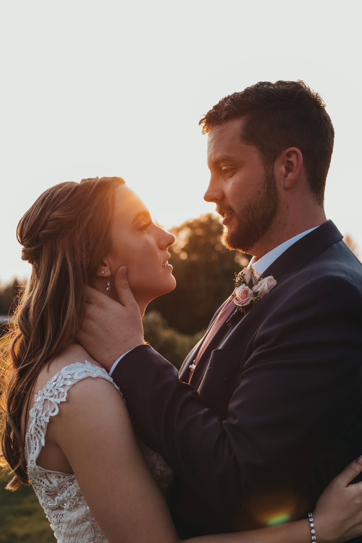 Bride and groom sharing romantic golden hour moment, groom tenderly holding brides face.