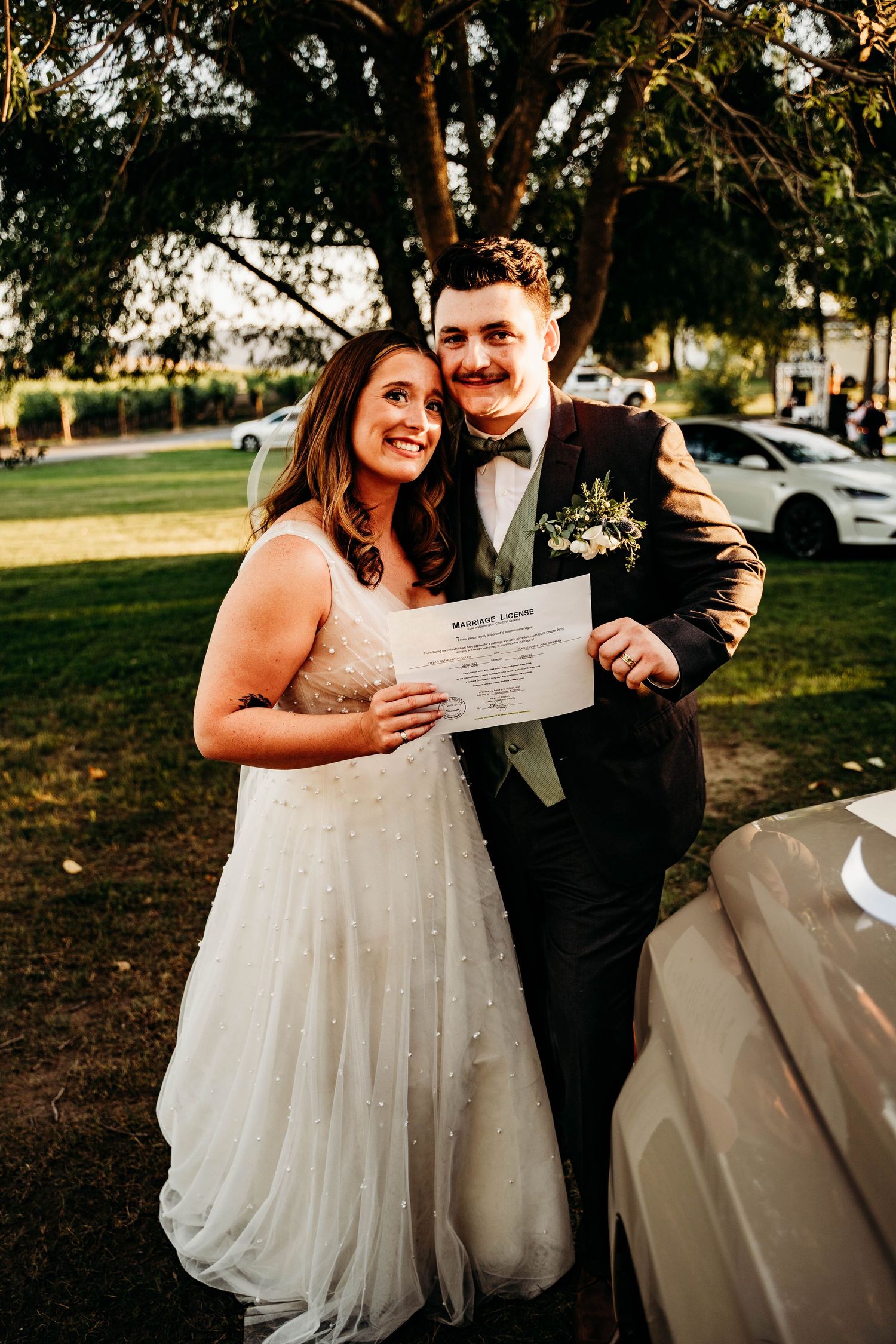 Smiling newlywed couple proudly holding their marriage license outdoors after their wedding ceremony.