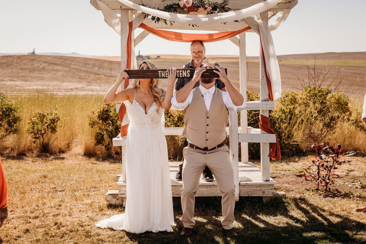 Bride and groom hold signs during outdoor rustic wedding ceremony.