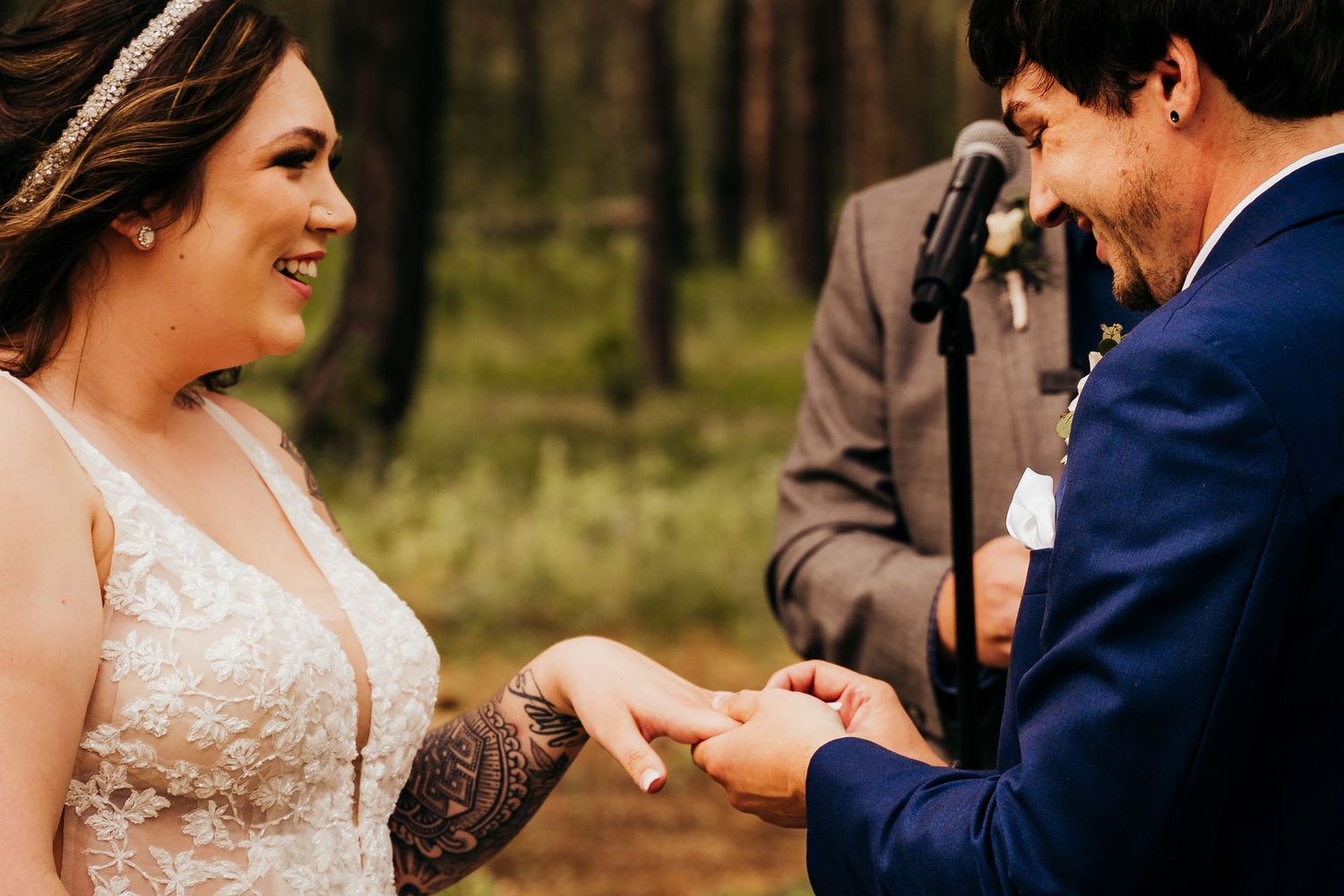 Bride with tattoos smiling as she places a ring on the grooms finger during ceremony.
