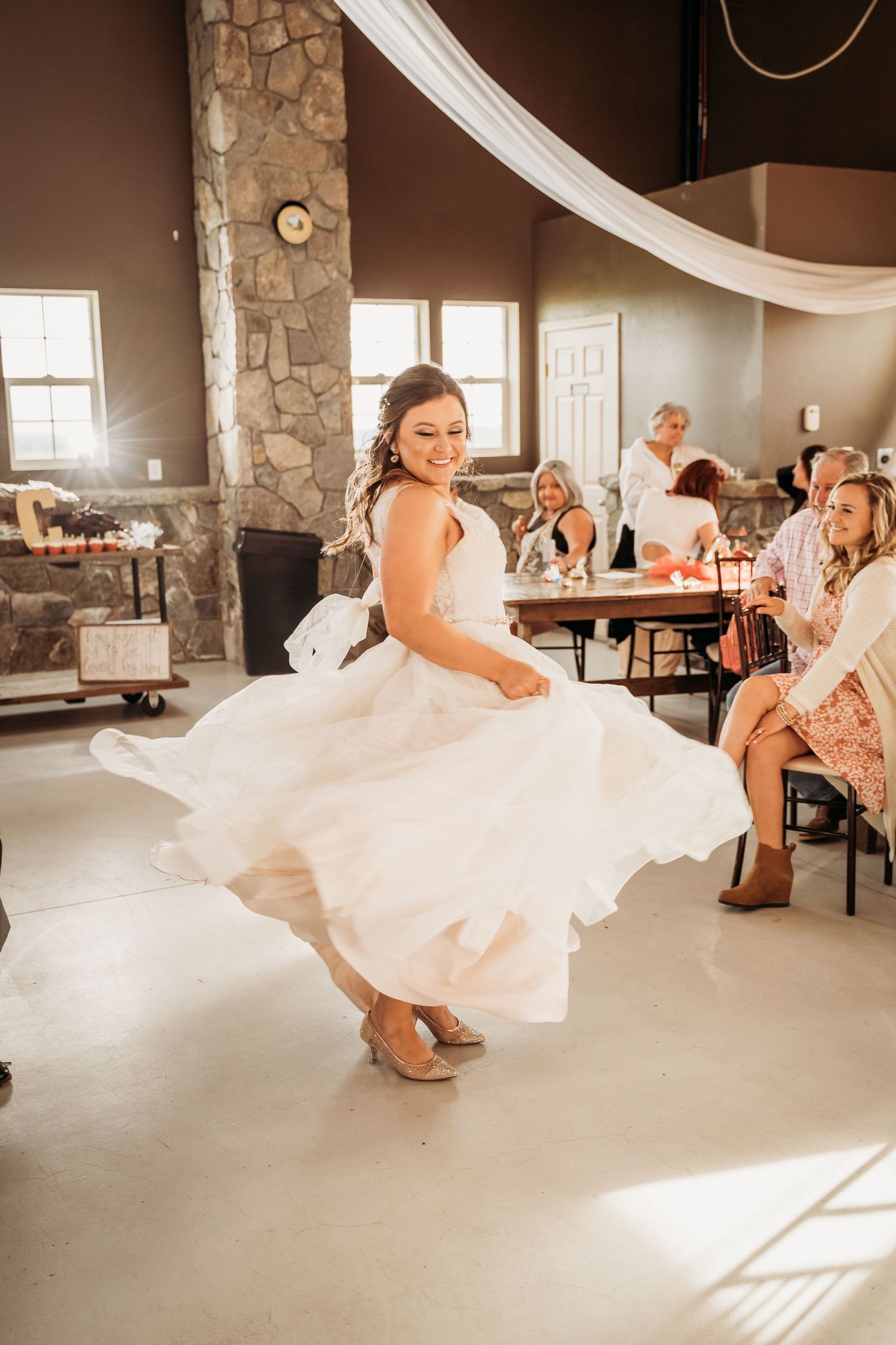 Bride in white ball gown twirling on dance floor at rustic wedding reception venue.