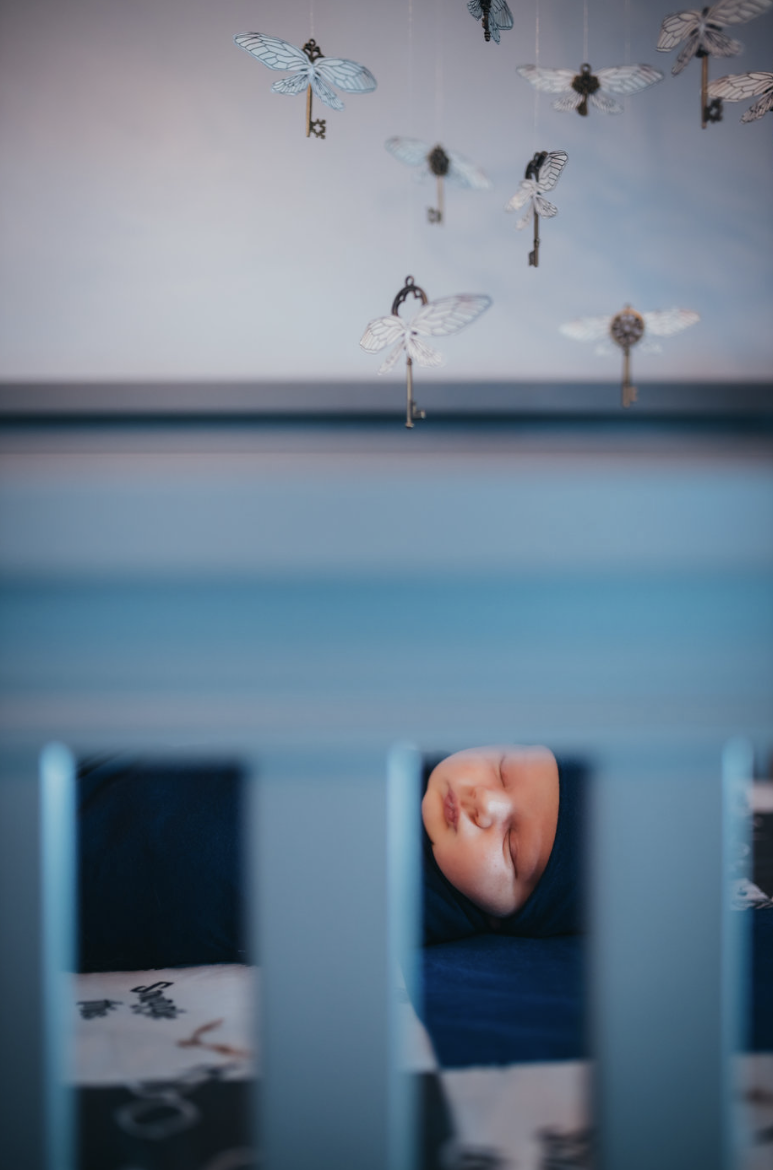Baby sleeping in blue crib with magical flying keys mobile hanging overhead.