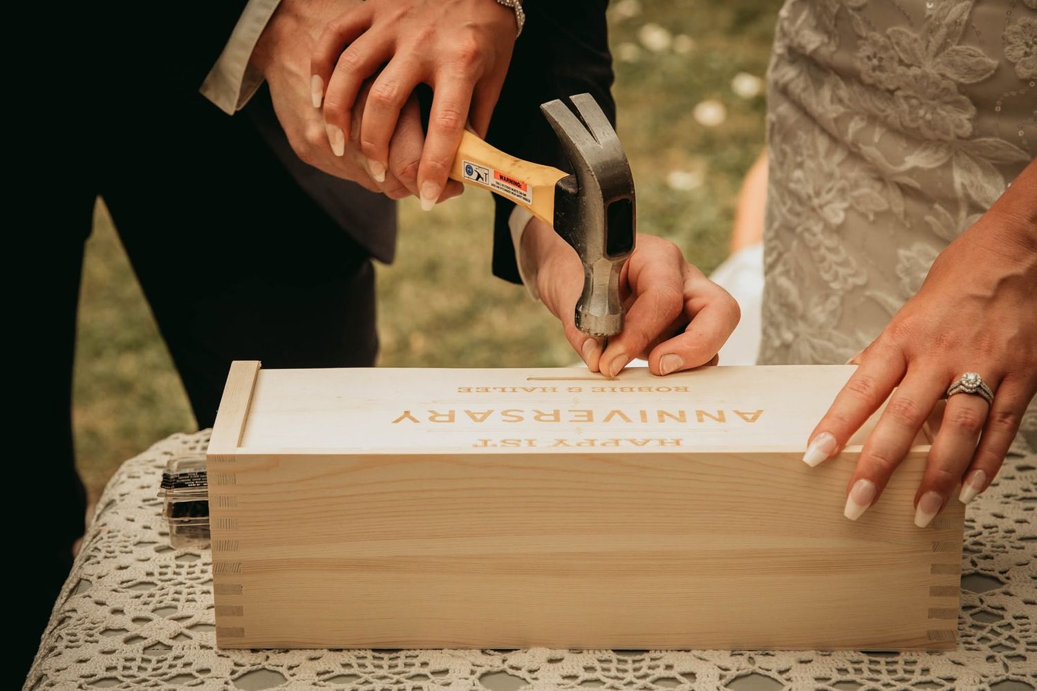 Bride and groom nailing shut a wooden anniversary wine box during wedding ceremony.