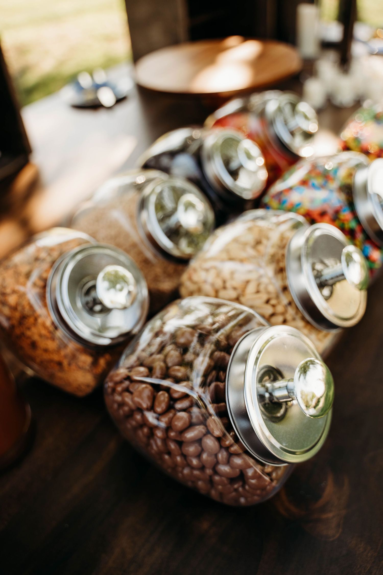 Glass jars with silver lids filled with coffee beans and mixed candies displayed on a wooden table.