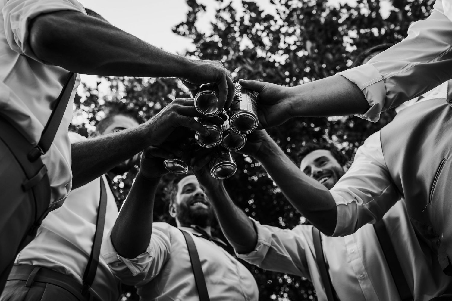 Groomsmen toast with drinks in black and white wedding celebration photo.
