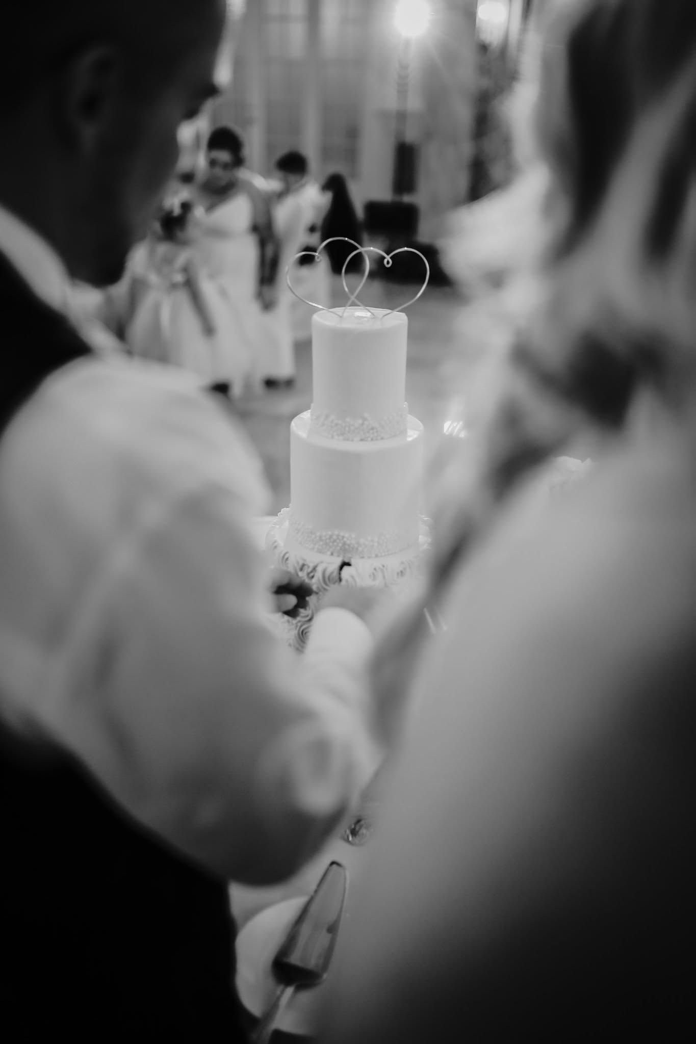 Bride and groom cutting elegant two-tier white wedding cake with heart topper.