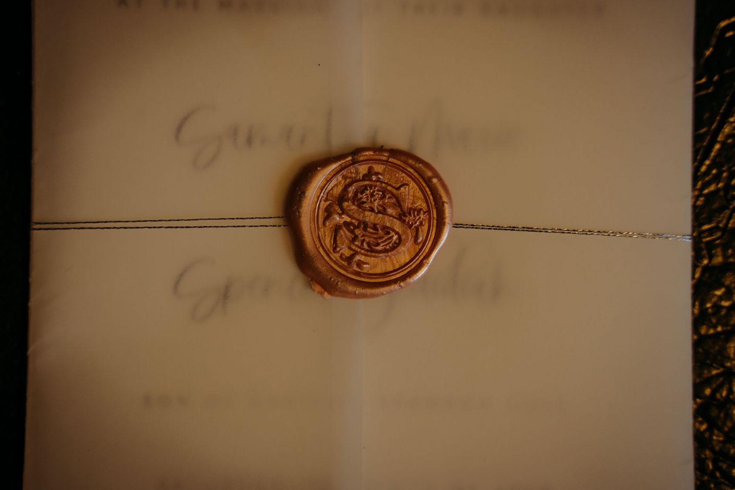 Elegant wedding invitation sealed with a copper wax seal featuring ornate monogram initials.