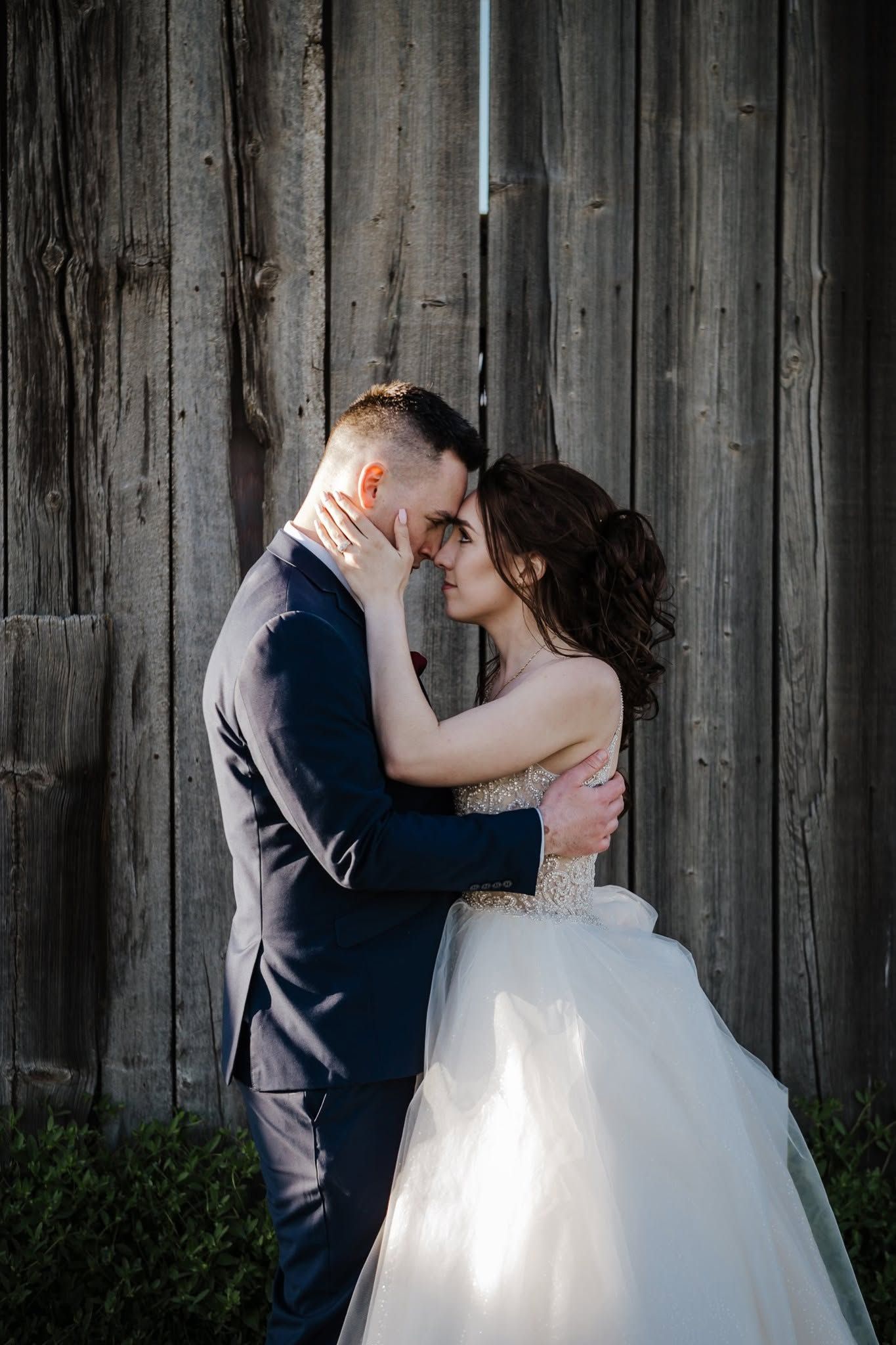 Bride and groom share an intimate moment against a rustic wooden barn wall at wedding.