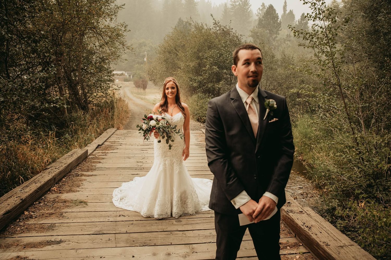 Bride and groom first look moment on a wooden bridge surrounded by misty forest.