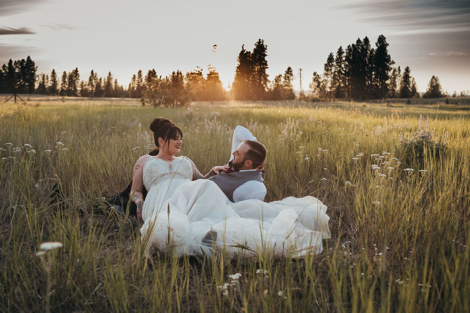Bride and groom relax together in a wildflower meadow during a romantic golden sunset photo session.