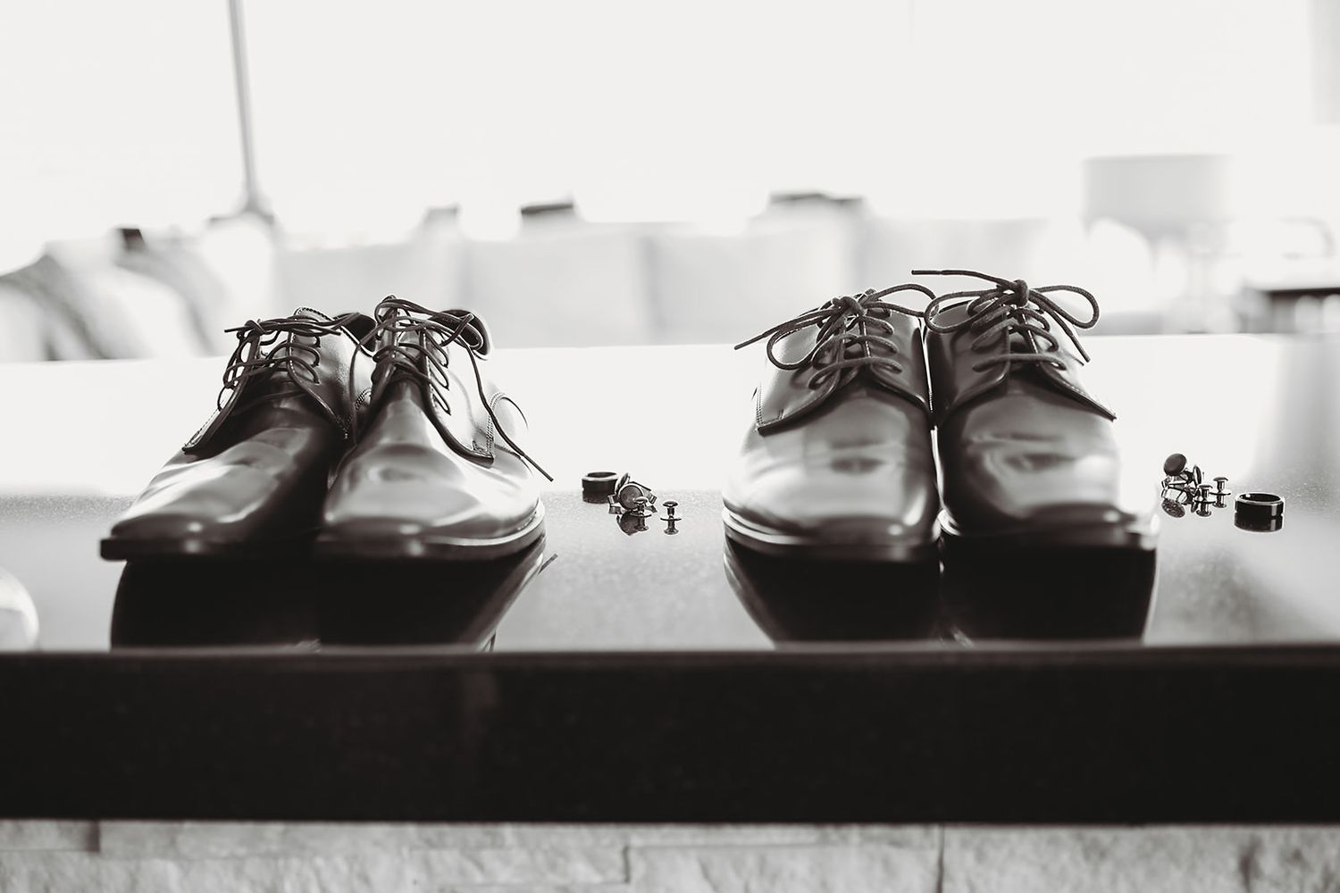 Classic brown leather dress shoes and cufflinks displayed on a table in black and white.