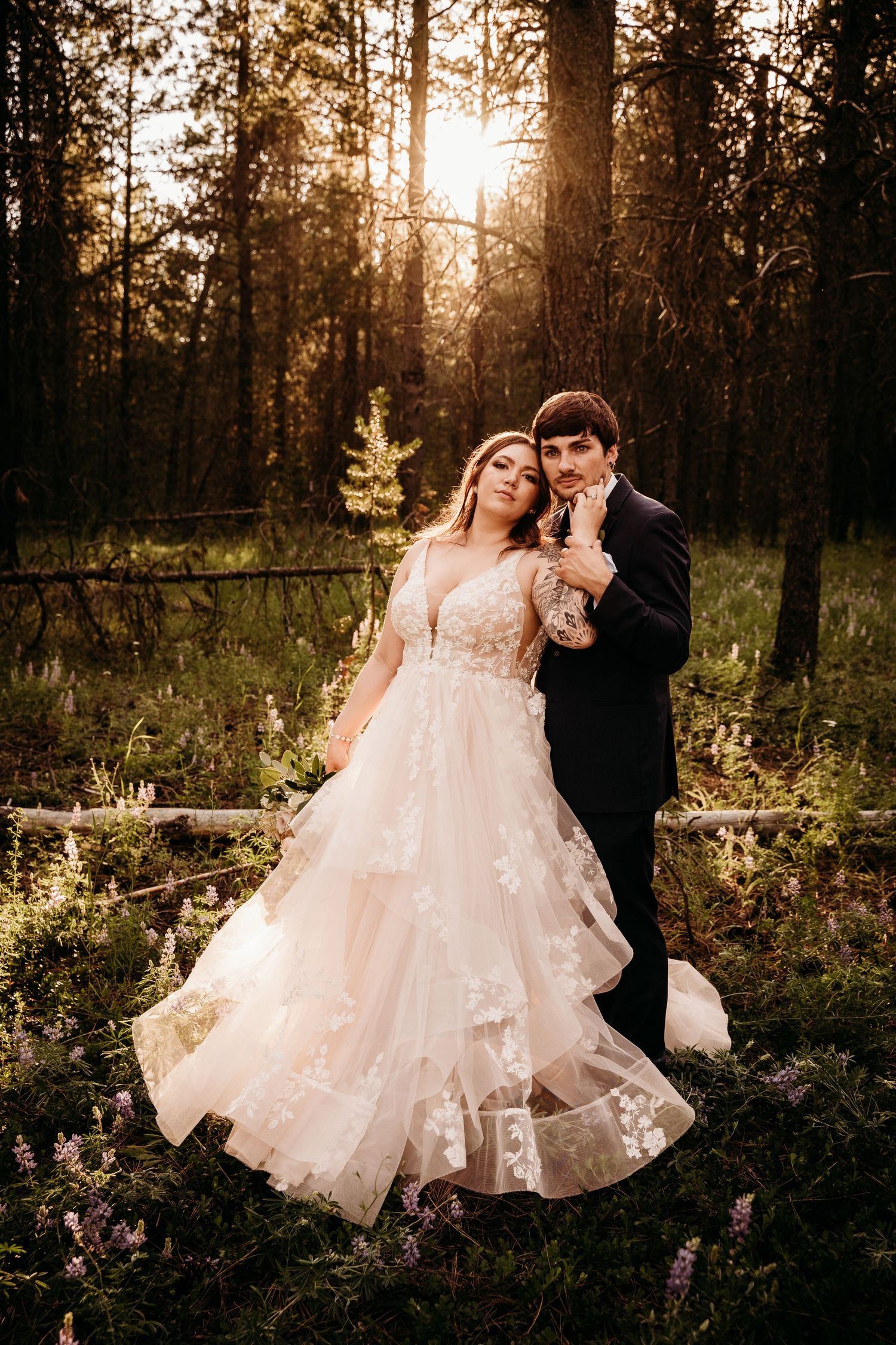 Bride in a floral ballgown and groom pose together in a wildflower forest at golden sunset.