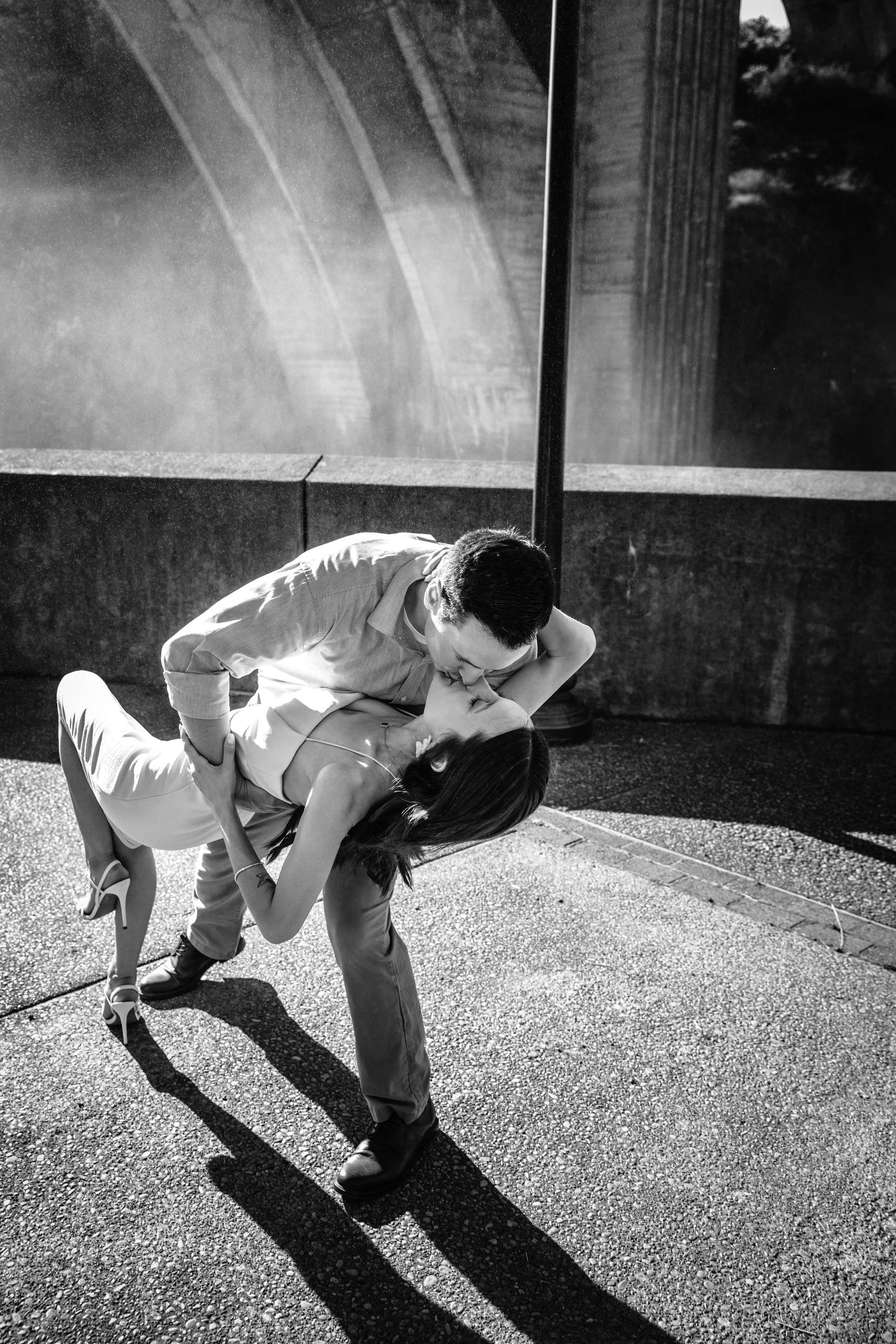 Couple sharing a romantic dip kiss in black and white outdoor photography.