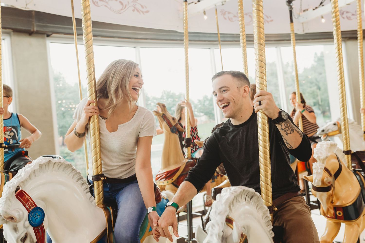 Happy couple laughing together while riding carousel horses at indoor amusement ride.