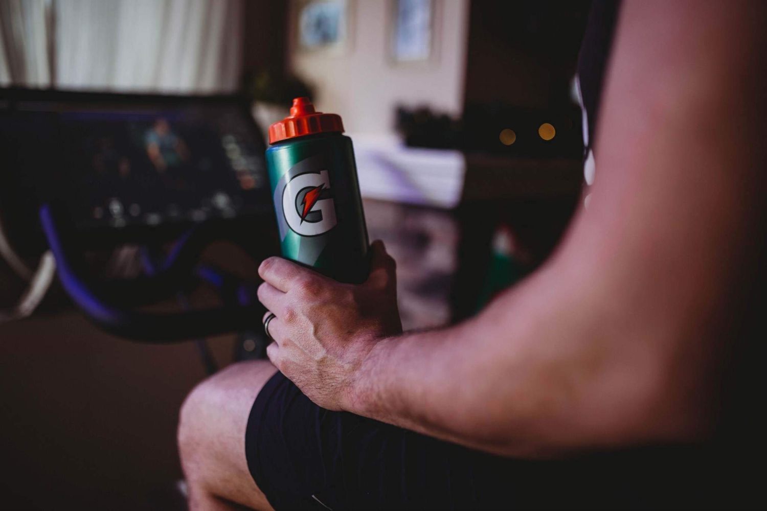 Athlete holding a green Gatorade water bottle while sitting near gym equipment.