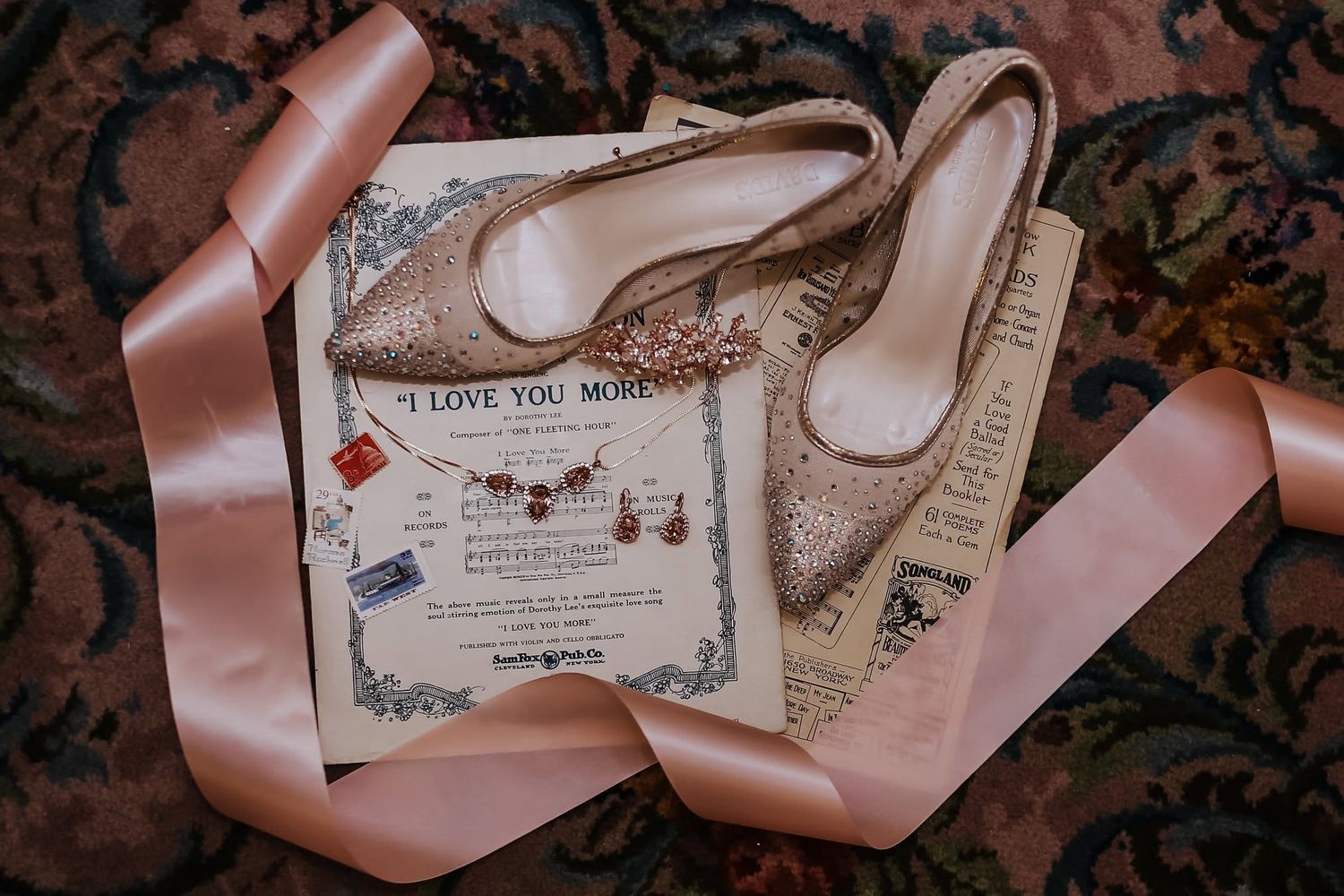 Rose gold glitter bridal heels with jewelry and sheet music wedding flat lay.
