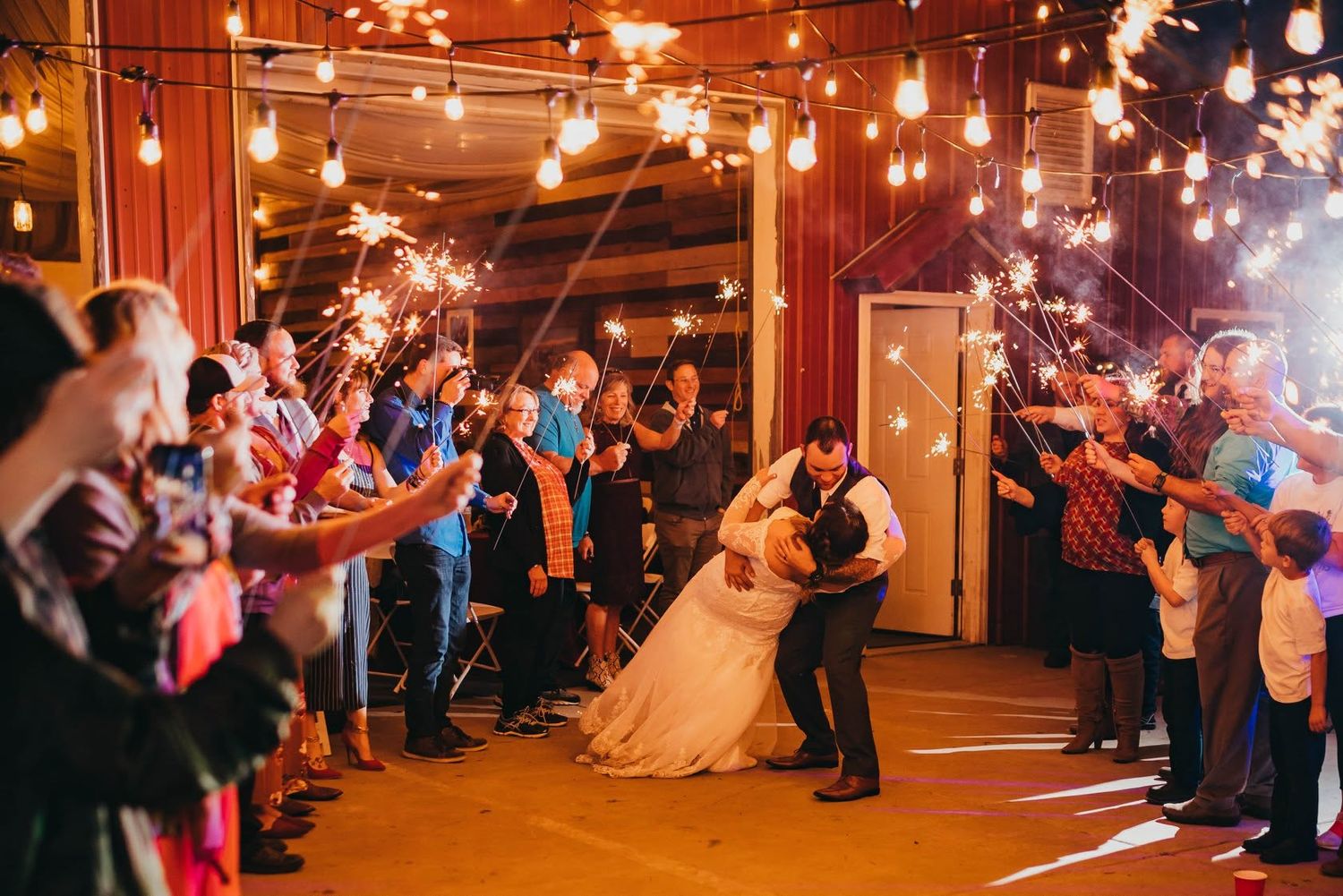 Bride and groom share a first dance surrounded by sparklers at indoor barn wedding reception.
