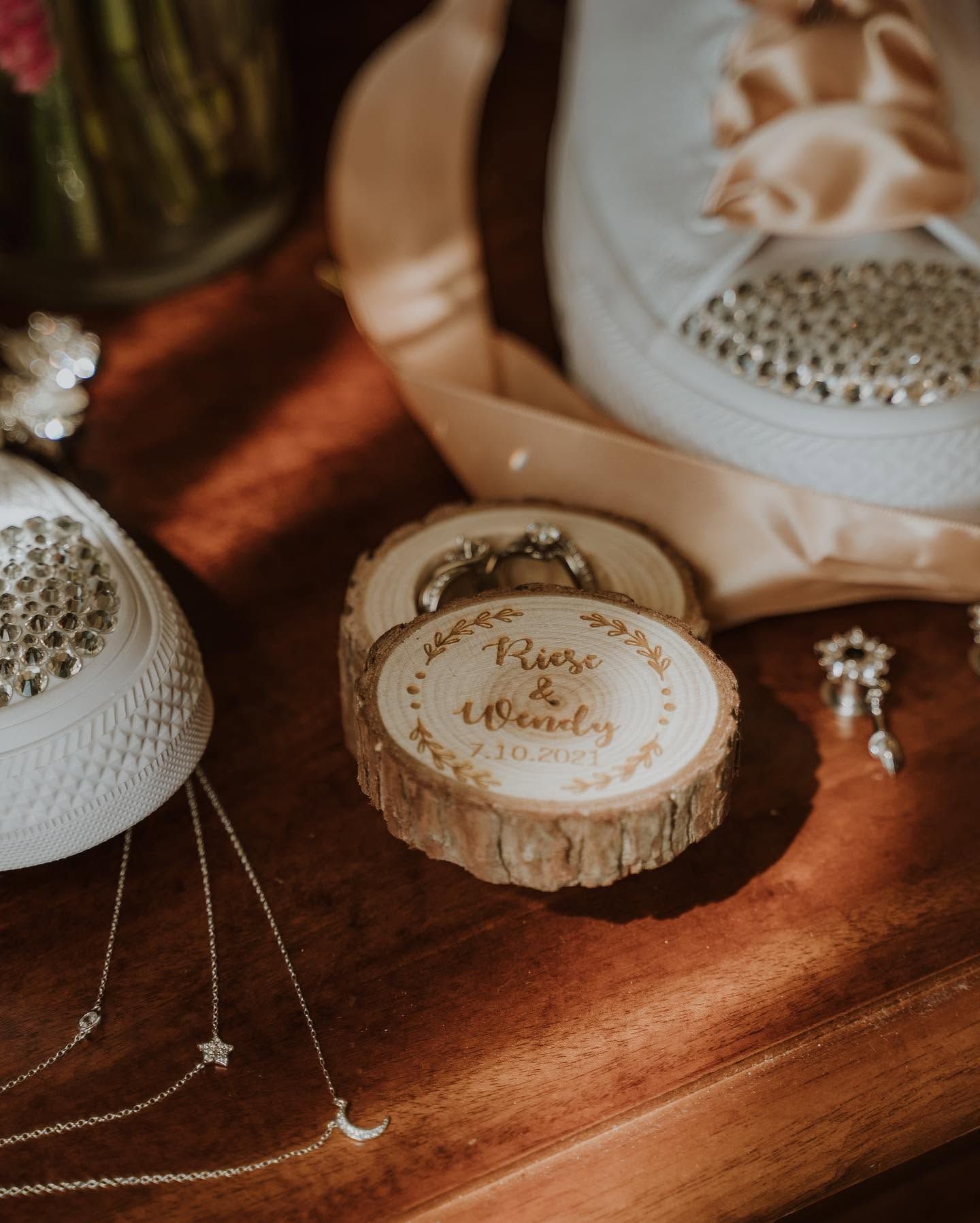 Rustic wooden slice ring box engraved with bride and groom names displayed on a wooden table with jewelry.