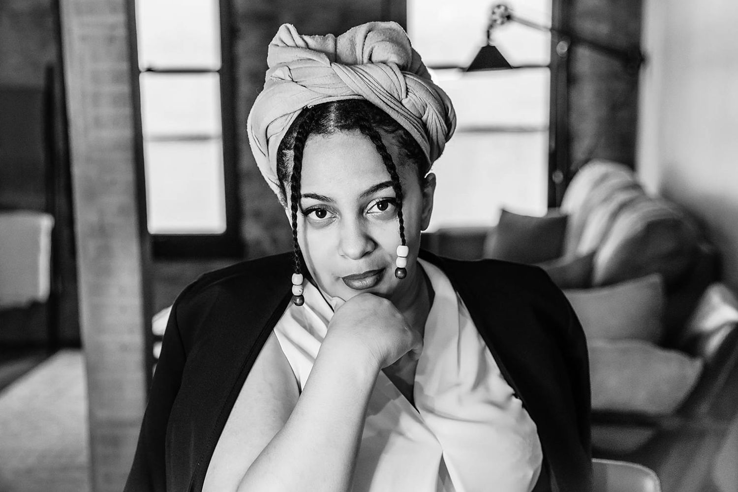 Black and white portrait of a woman with a towel turban resting her chin on her hands indoors.