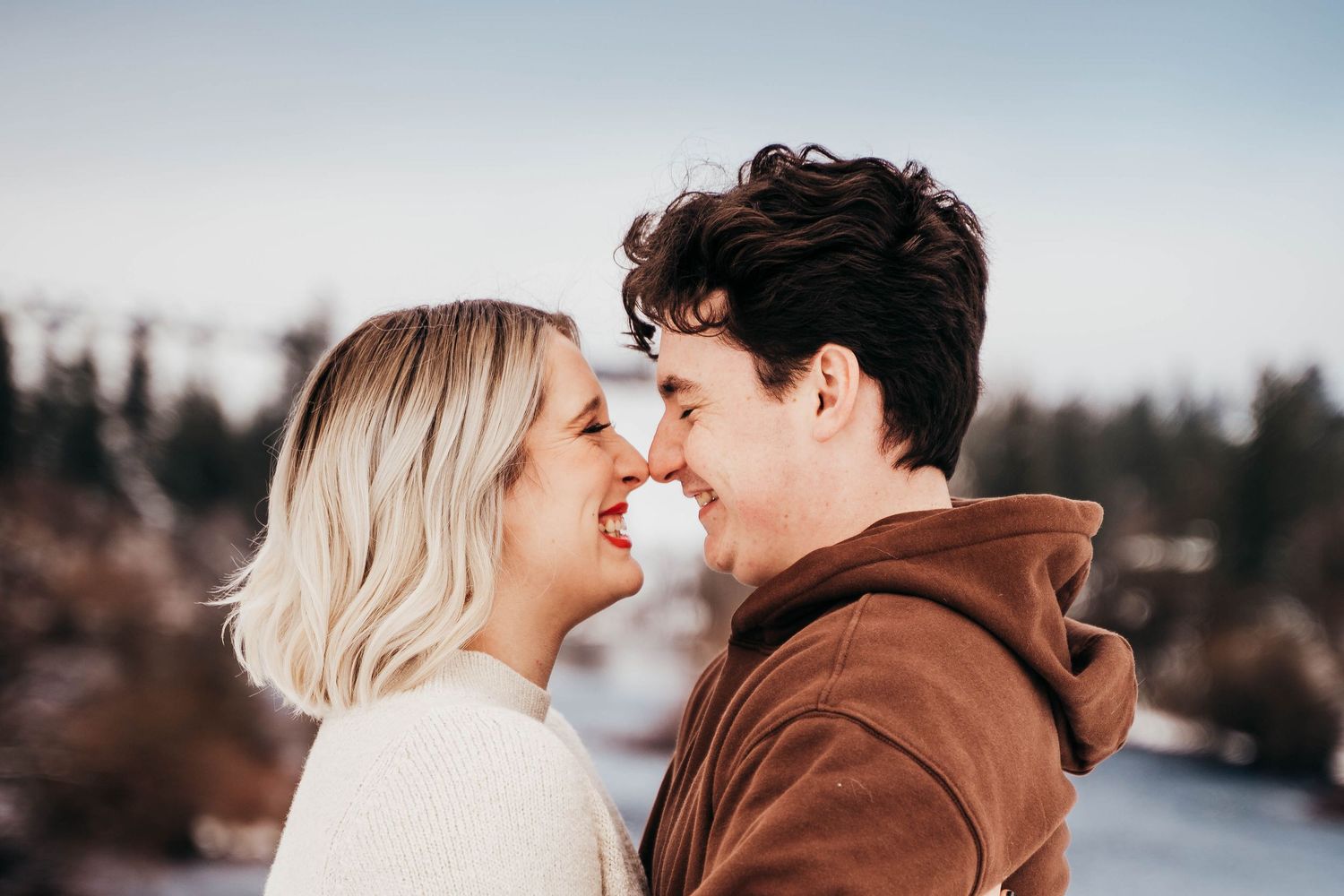 Happy couple smiling and touching foreheads in romantic winter outdoor engagement photo.