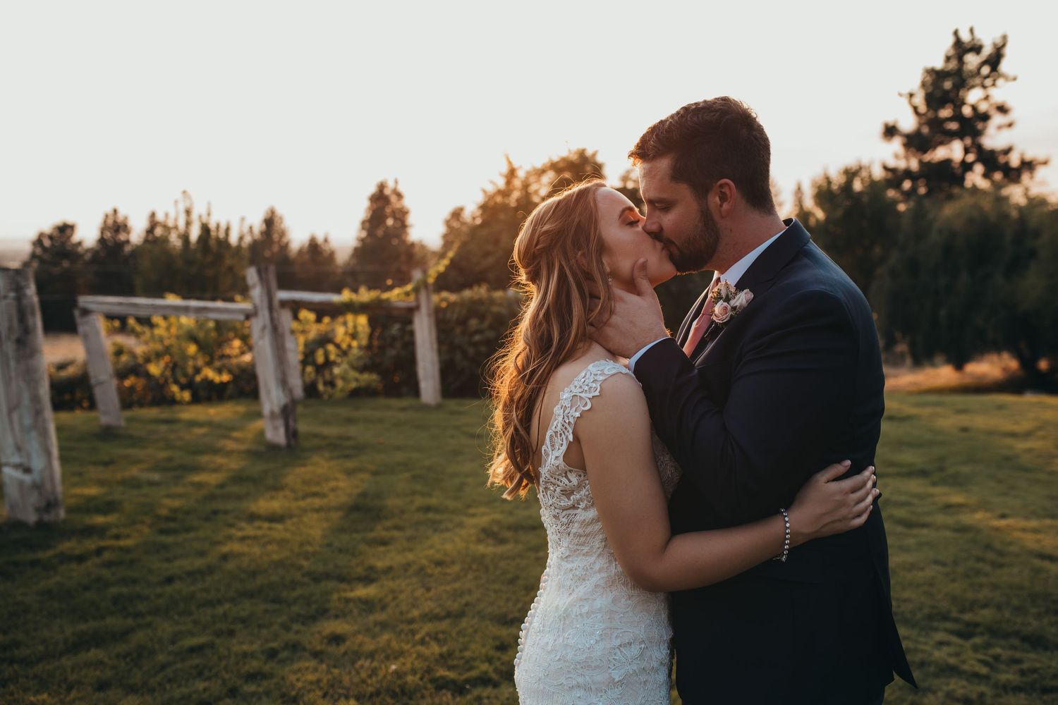 Bride and groom share a tender kiss in a green field during their golden hour wedding photos.