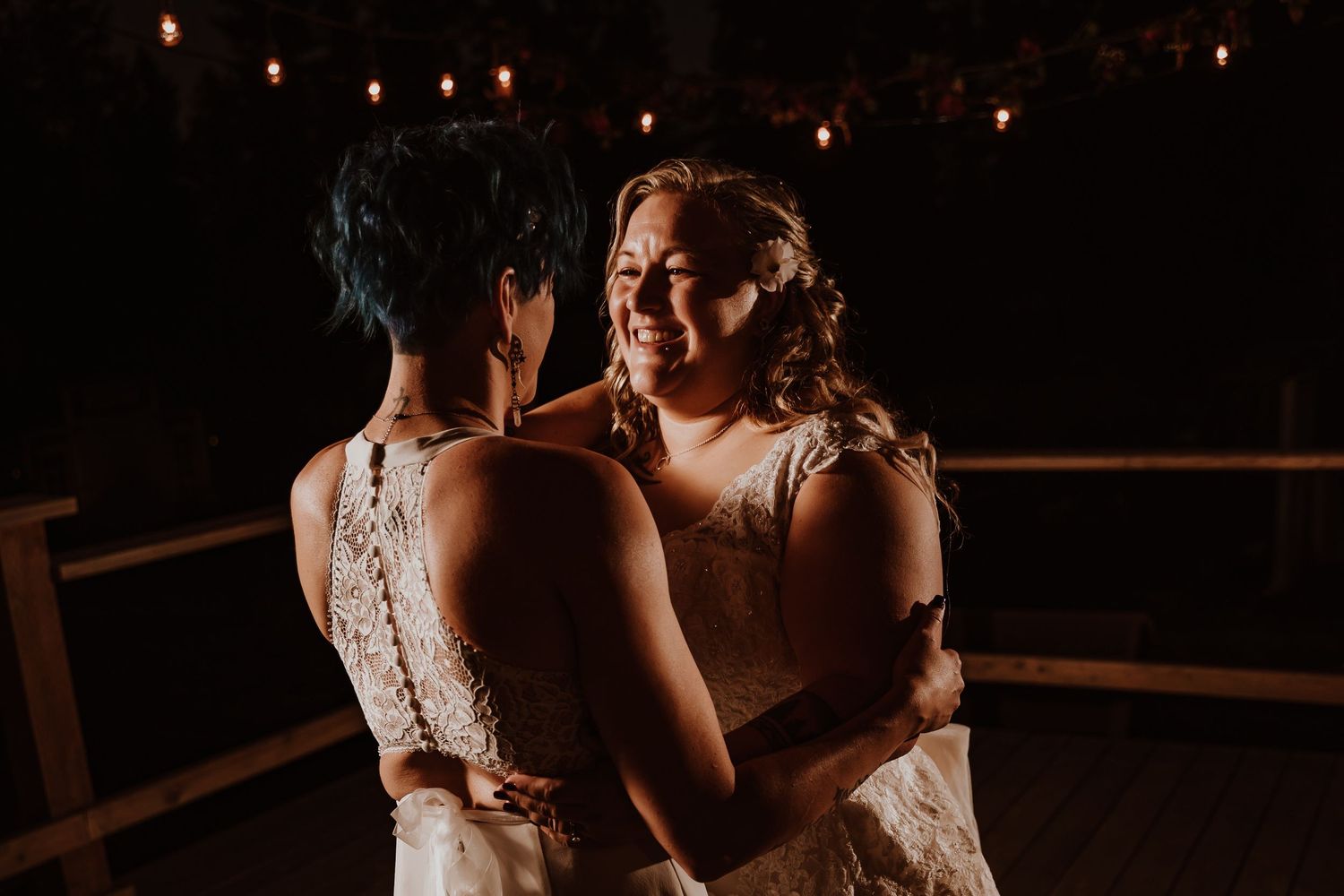 Two brides share an intimate first dance under string lights at their wedding reception.