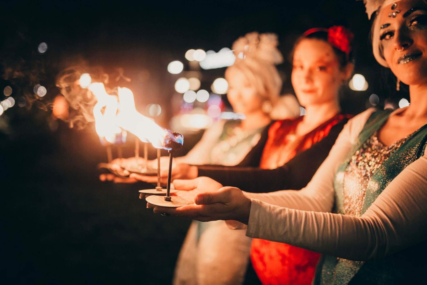 Women in costumes holding fire torches during nighttime performance event outdoors.