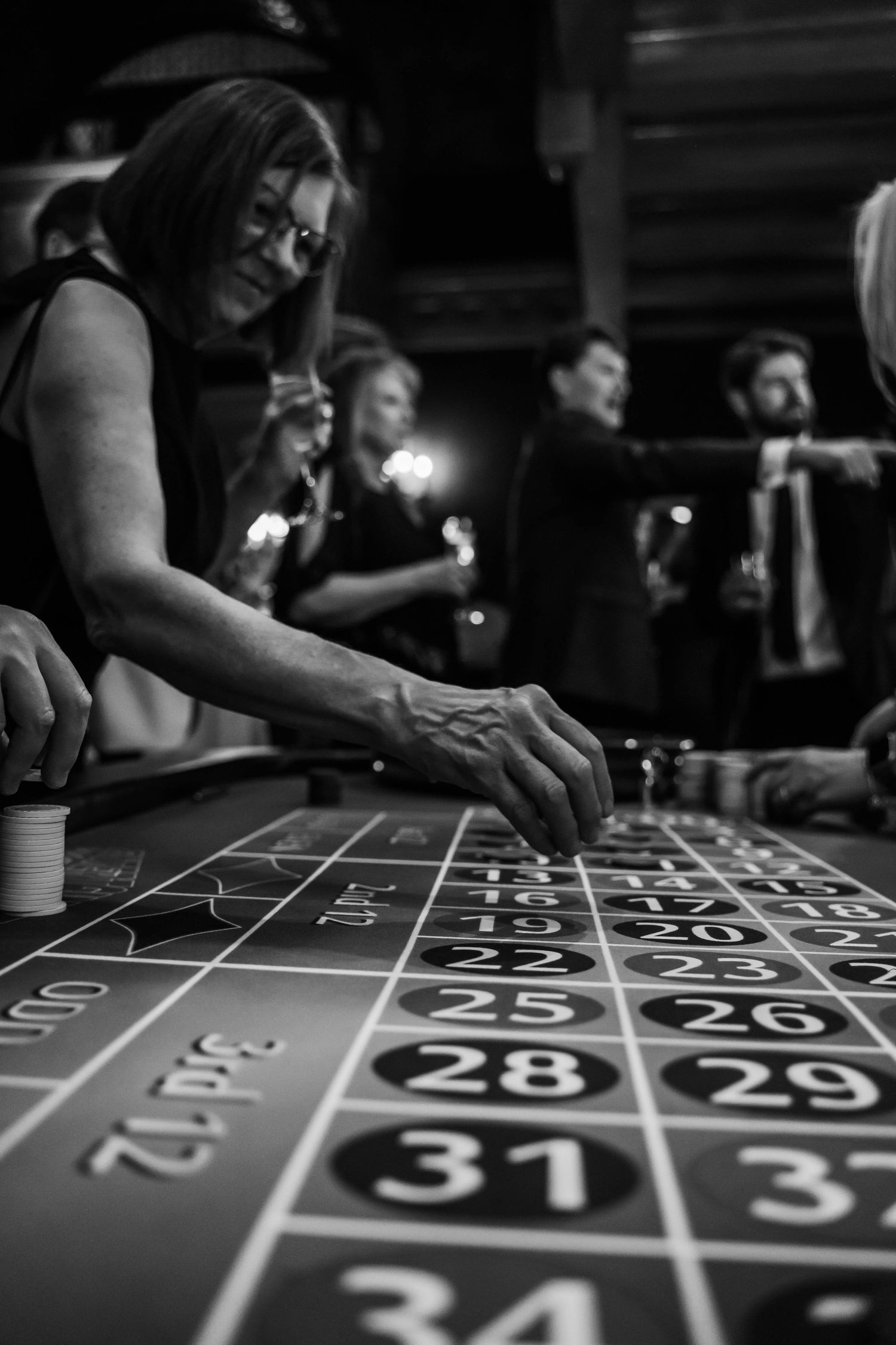 Black and white photo of a woman placing chips on a roulette table at a wedding reception casino night.