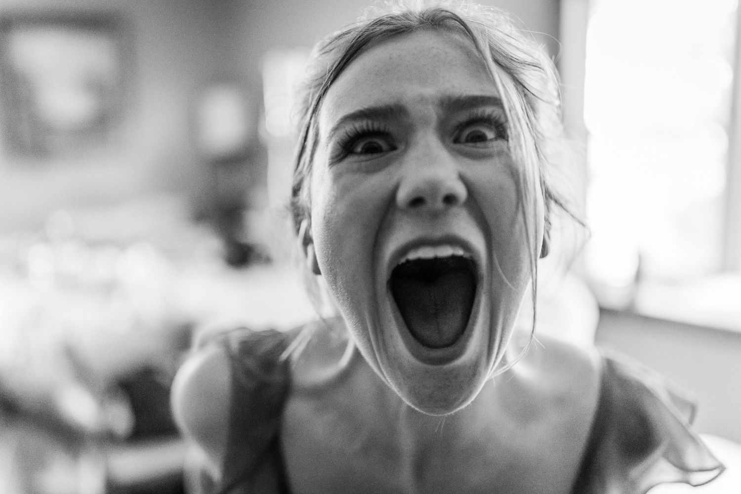 Bride reacts with joyful scream in candid black and white wedding photo.