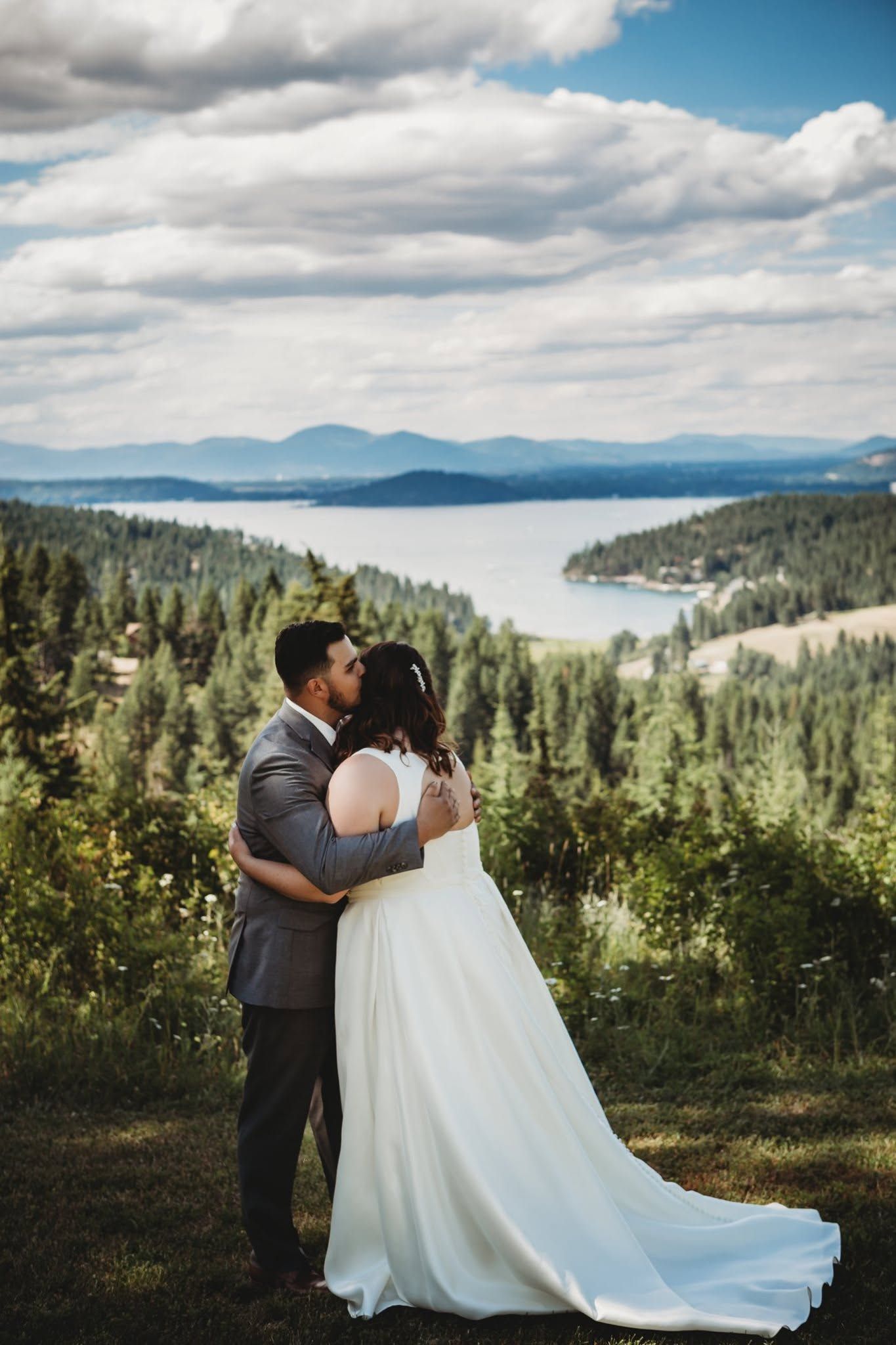 Bride and groom kissing with a stunning panoramic lake and forest view behind them.