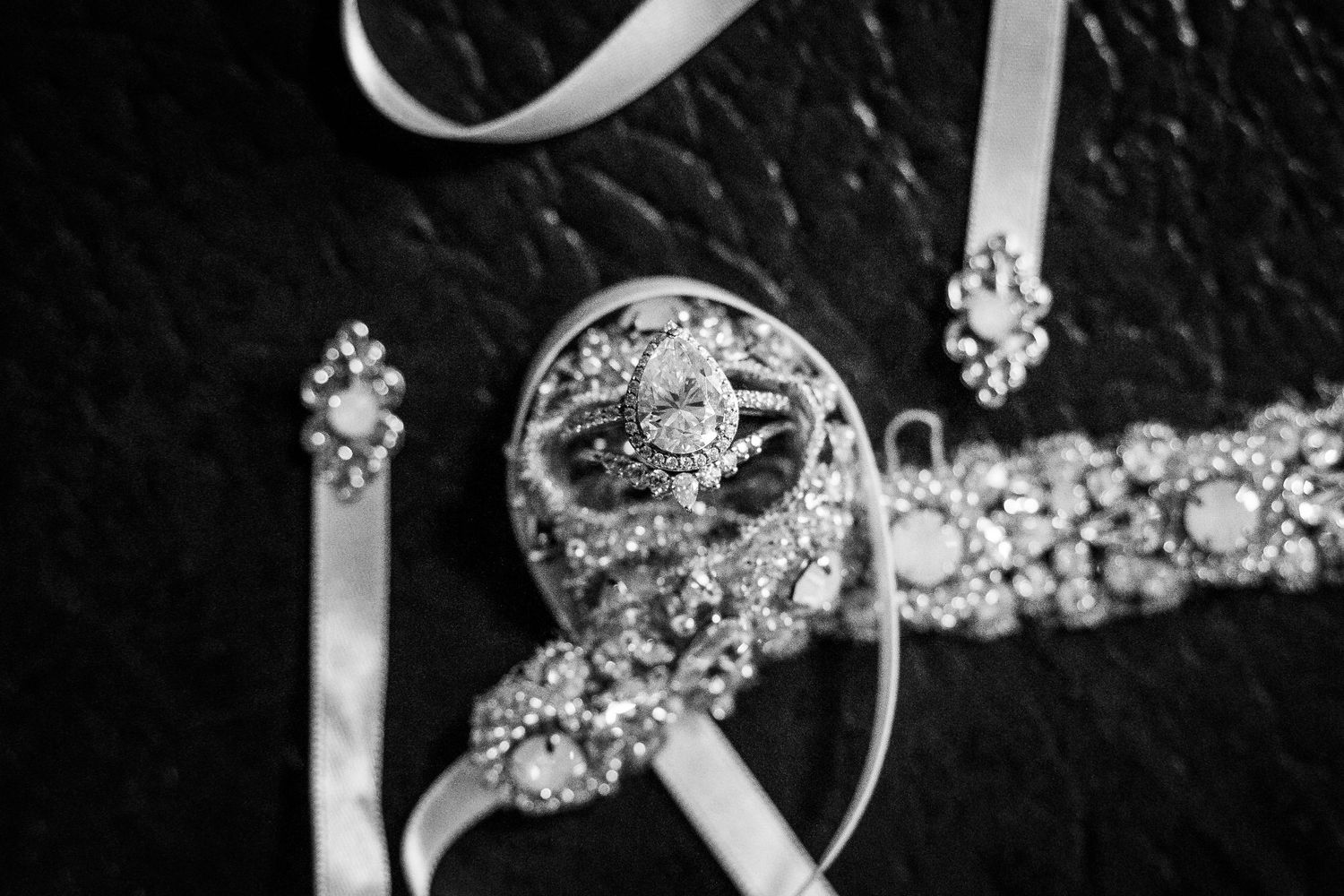 Black and white close-up of pear shaped diamond engagement ring with halo setting and wedding bands on ribbon.