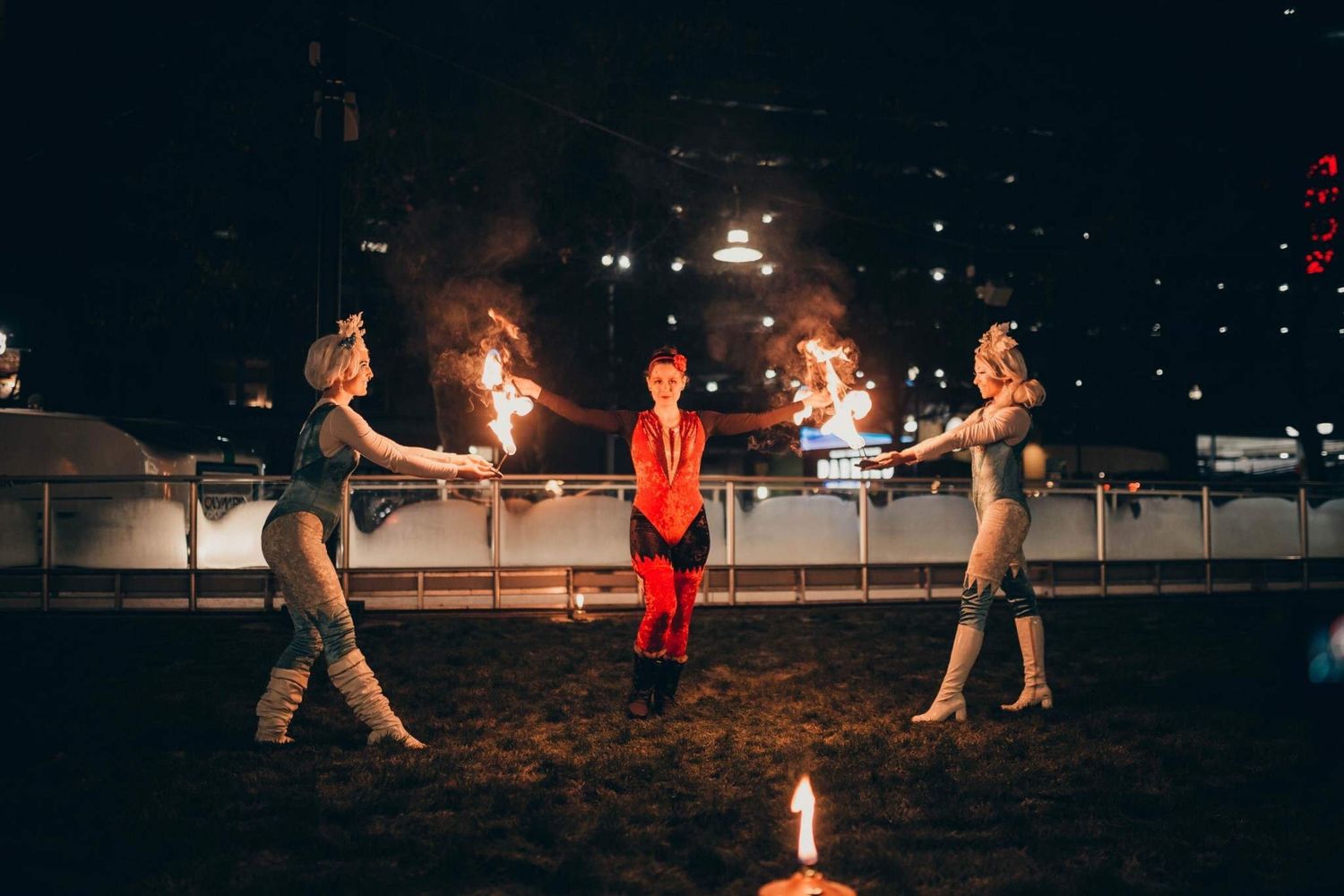 Fire performers in costumes spinning flames around child in red during nighttime outdoor show.
