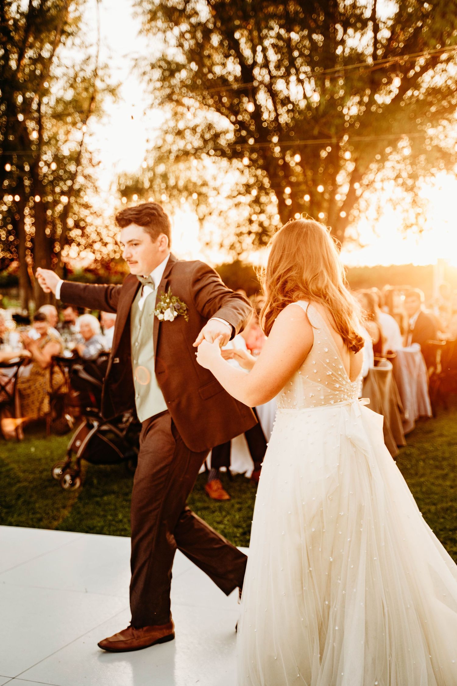 Groom energetically dances with bride on outdoor dance floor at golden hour reception.