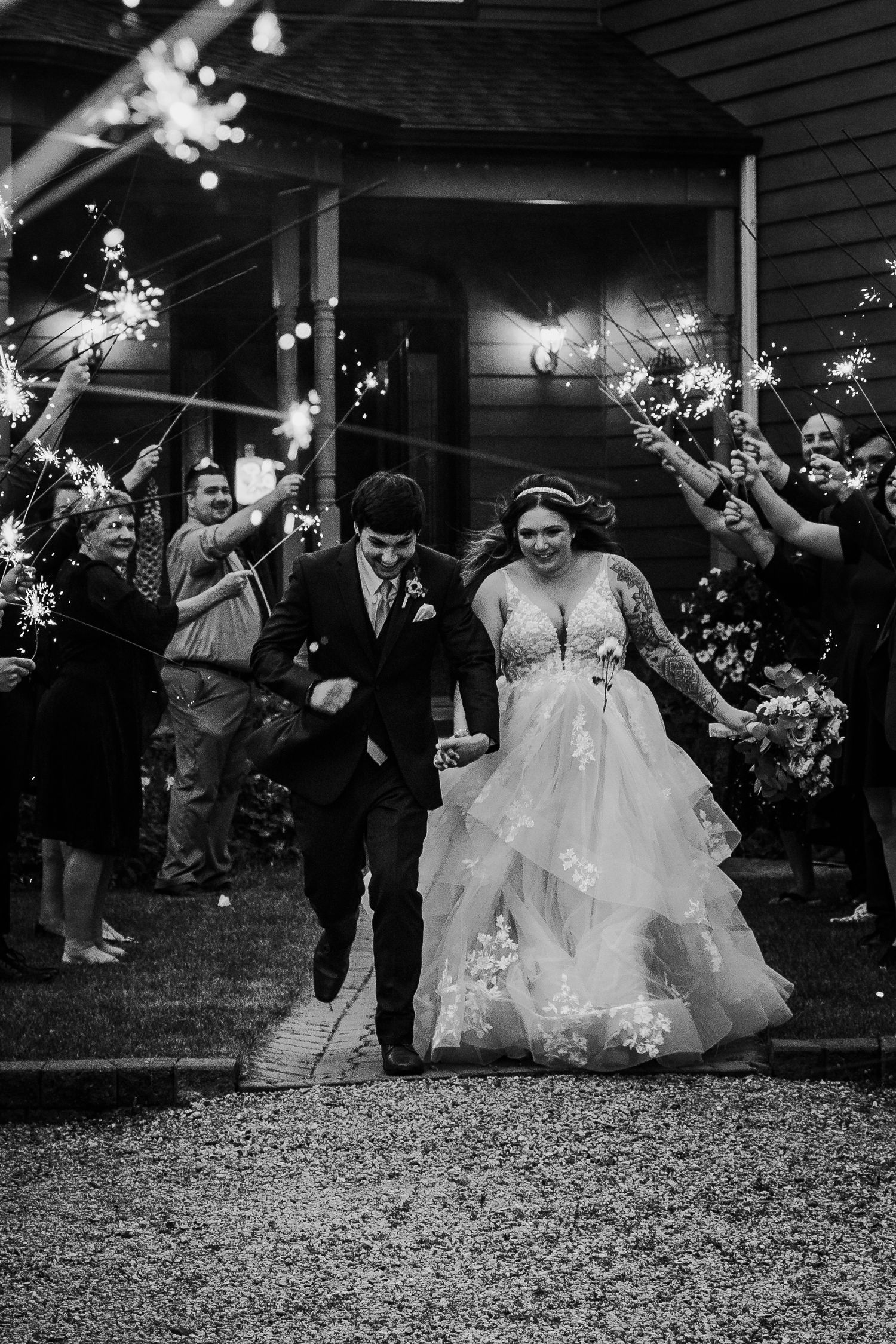 Black and white photo of bride and groom exiting through a sparkler send-off with cheering guests.