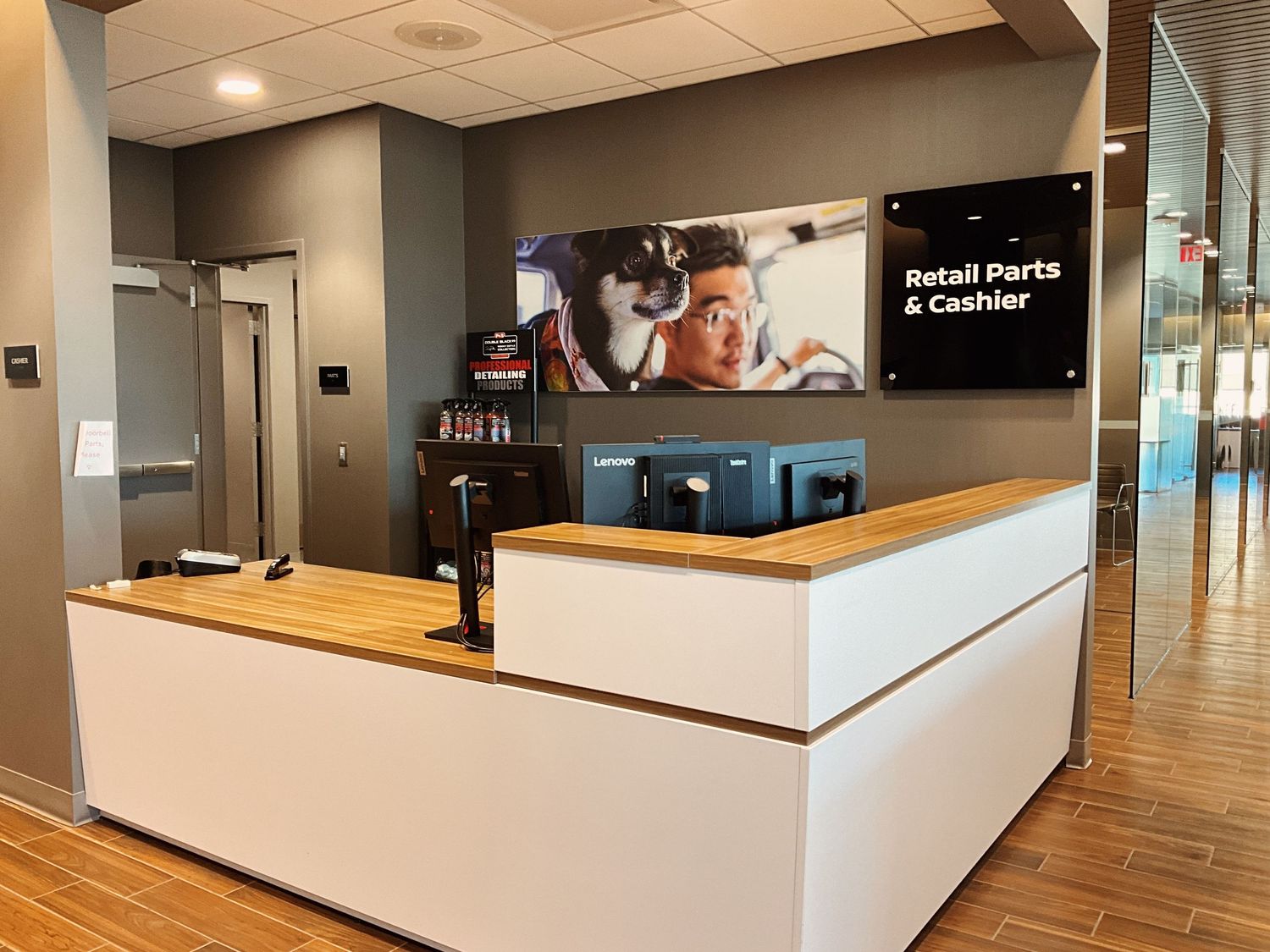 Modern dealership retail parts and cashier counter with white desk, wood accents, and digital display screen.
