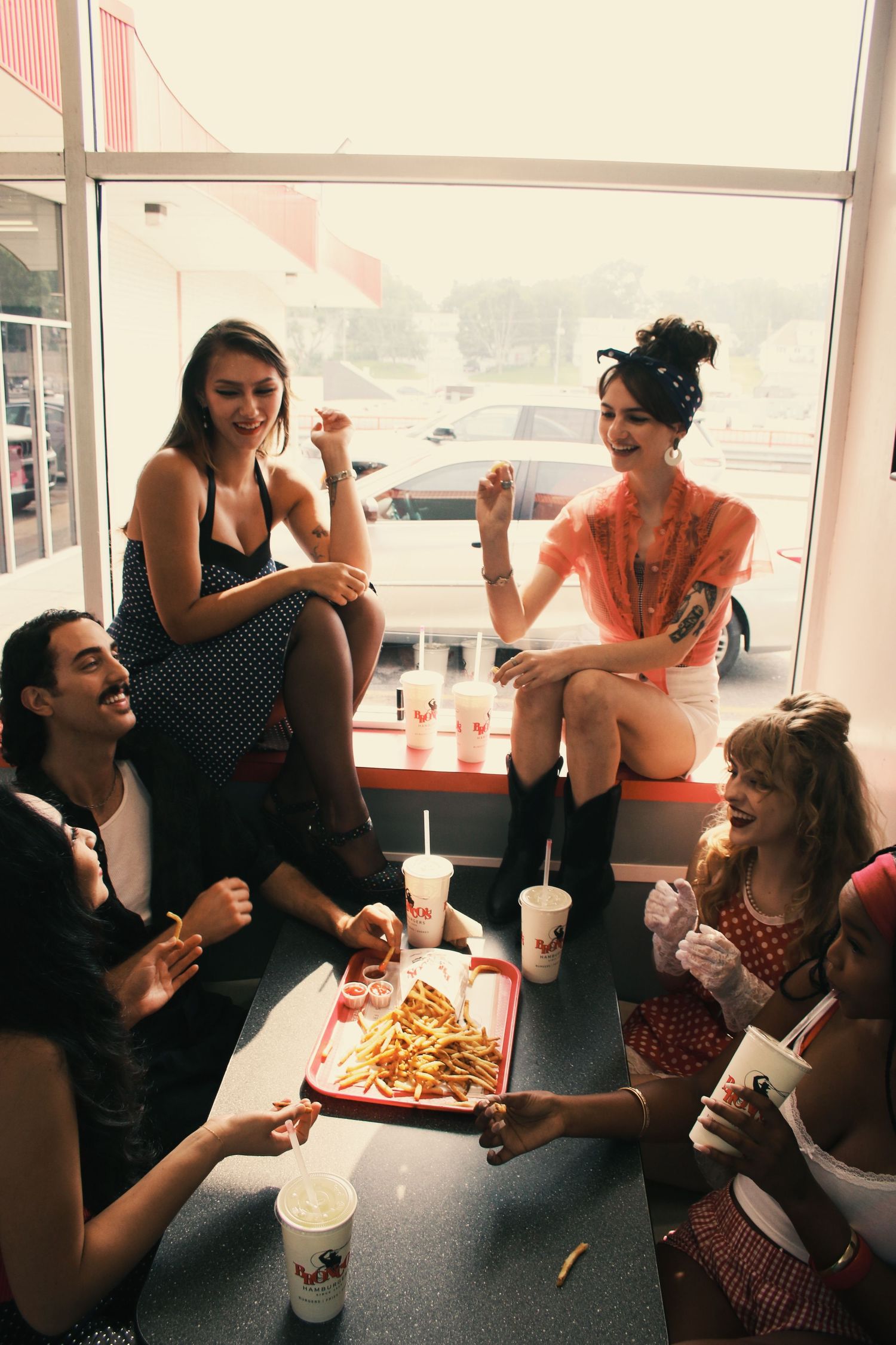 Group of friends sharing fries and milkshakes at a retro diner booth, laughing and enjoying a casual meal together.