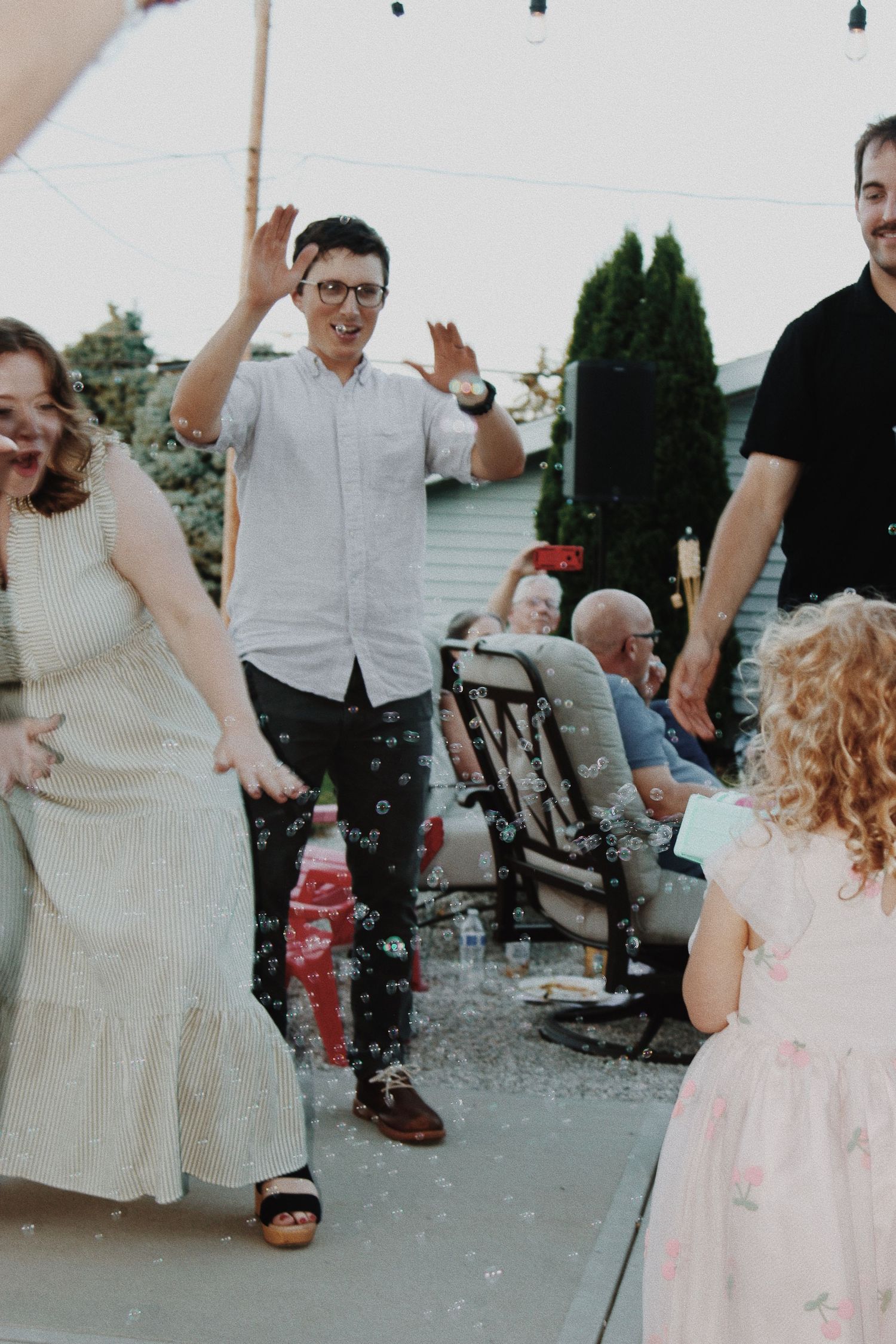 Guests dancing and playing with bubbles at an outdoor backyard party on a patio.
