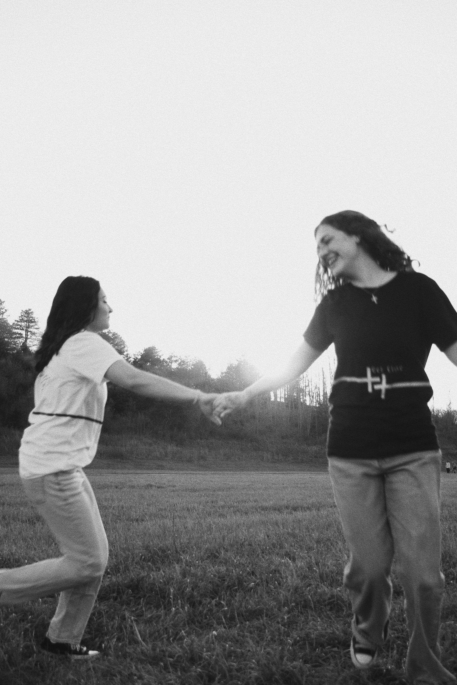 Two women holding hands and laughing in a black and white photo outdoors in a field.
