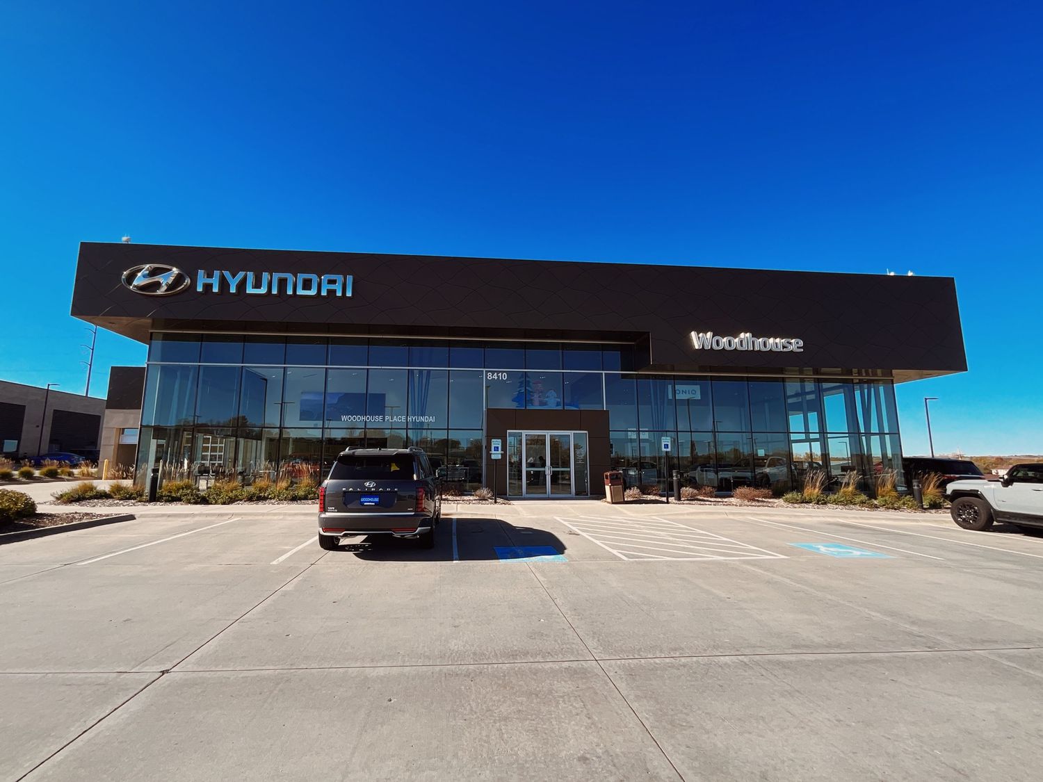 Modern Woodhouse Hyundai car dealership exterior with large glass facade, black signage, and spacious parking lot under blue sky.