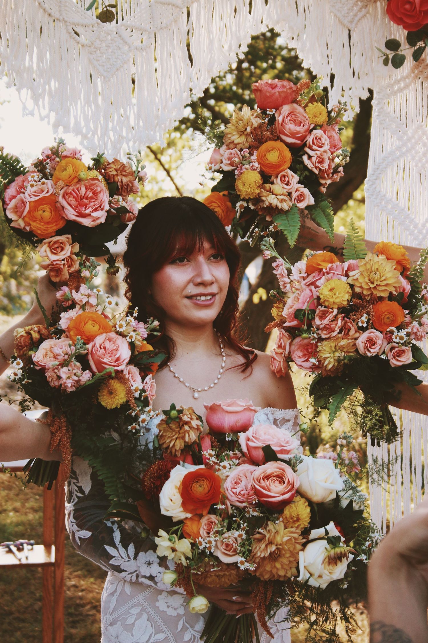 Bride surrounded by vibrant pink, orange, and yellow floral bouquets at an outdoor wedding ceremony.
