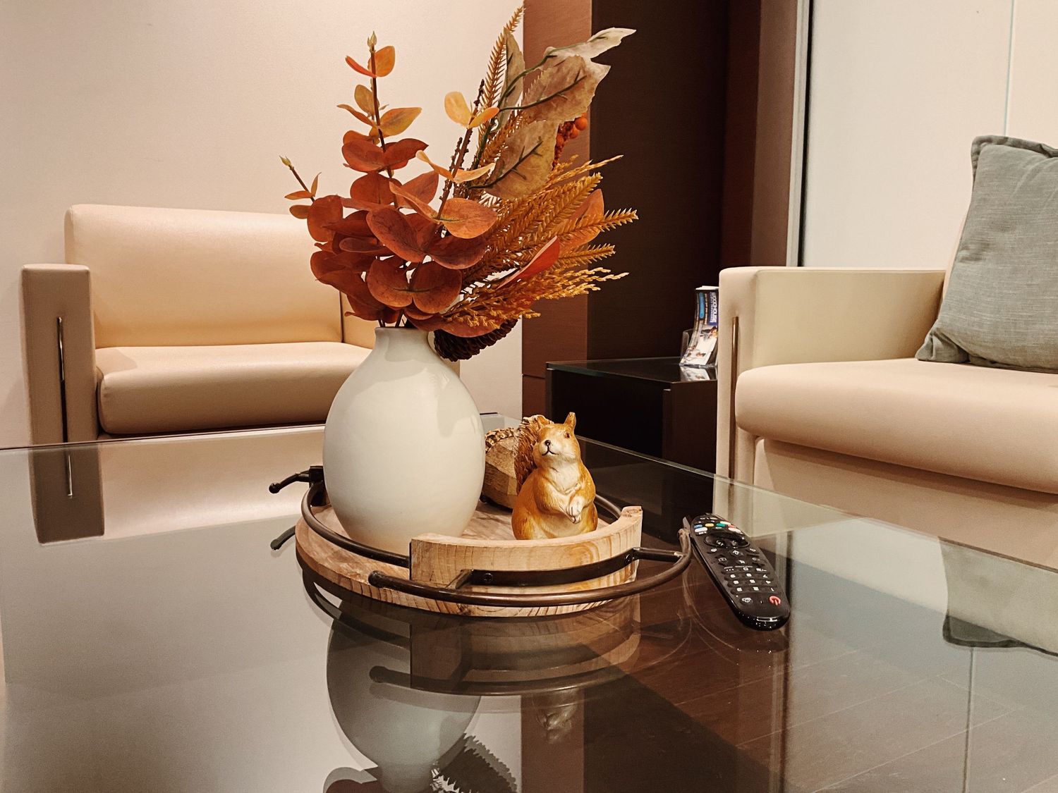 Elegant coffee table with white vase, autumn leaves, golden tiger figurine on tray, and remote control in modern living room.