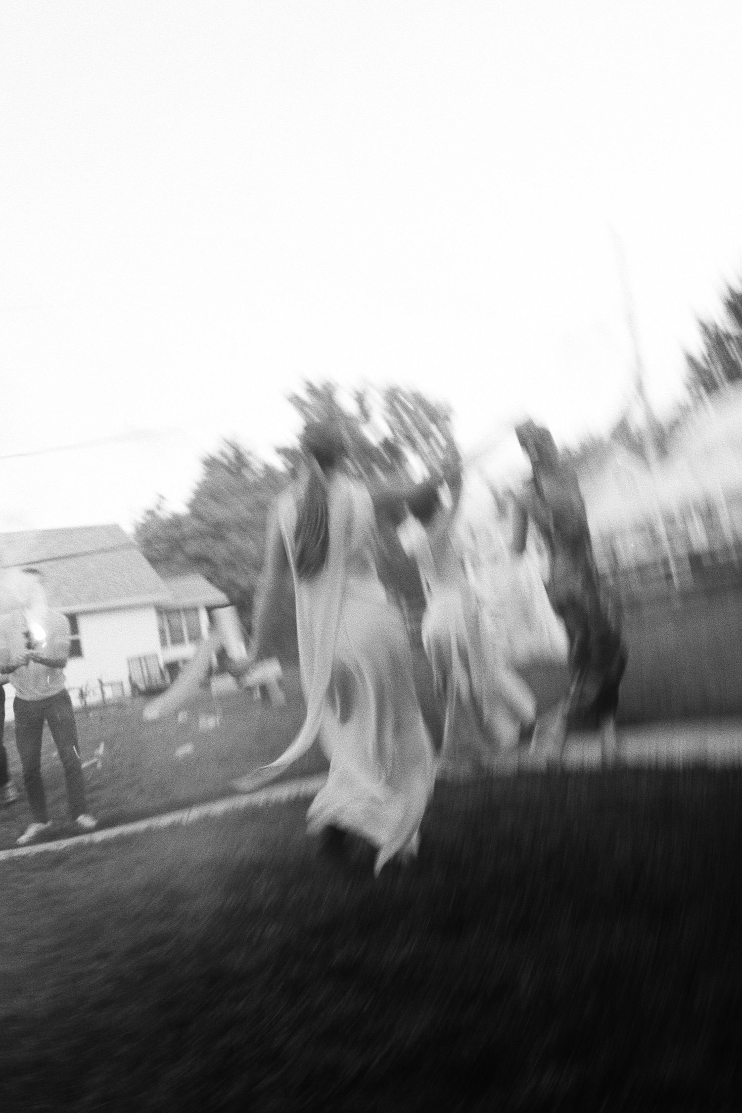 Blurry black and white photo of children playing outdoors near a house, captured with motion blur effect.