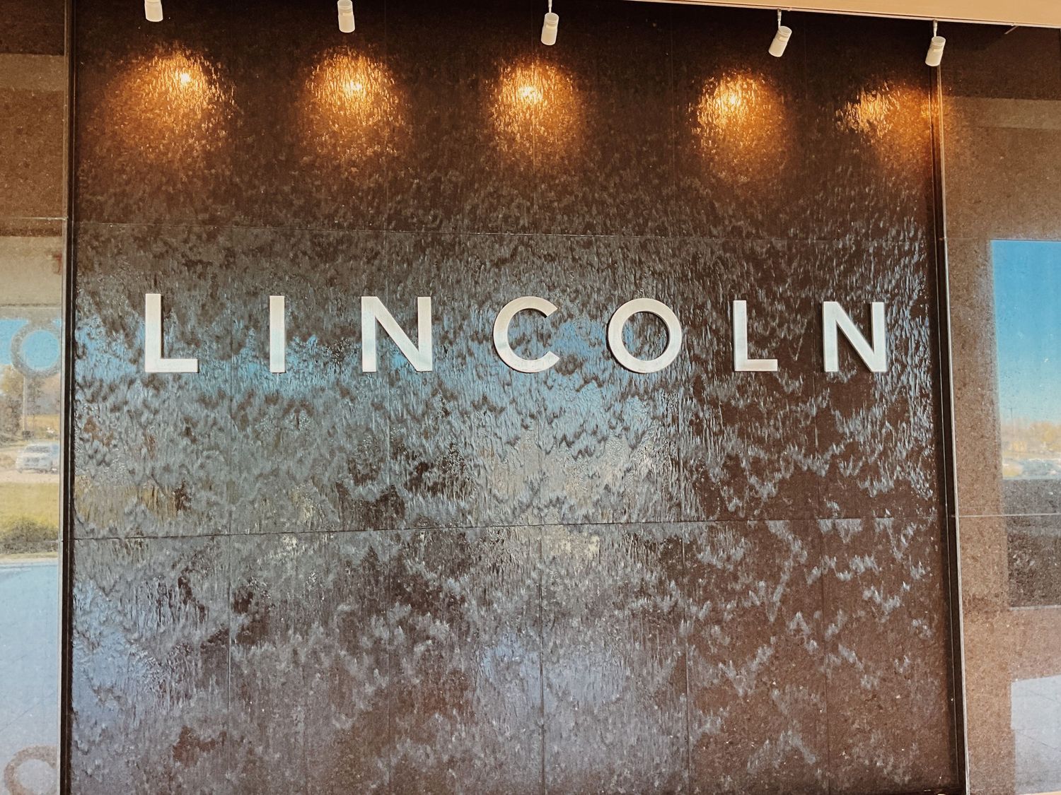 Illuminated Lincoln brand logo sign on a dark textured wall inside a luxury car dealership showroom.