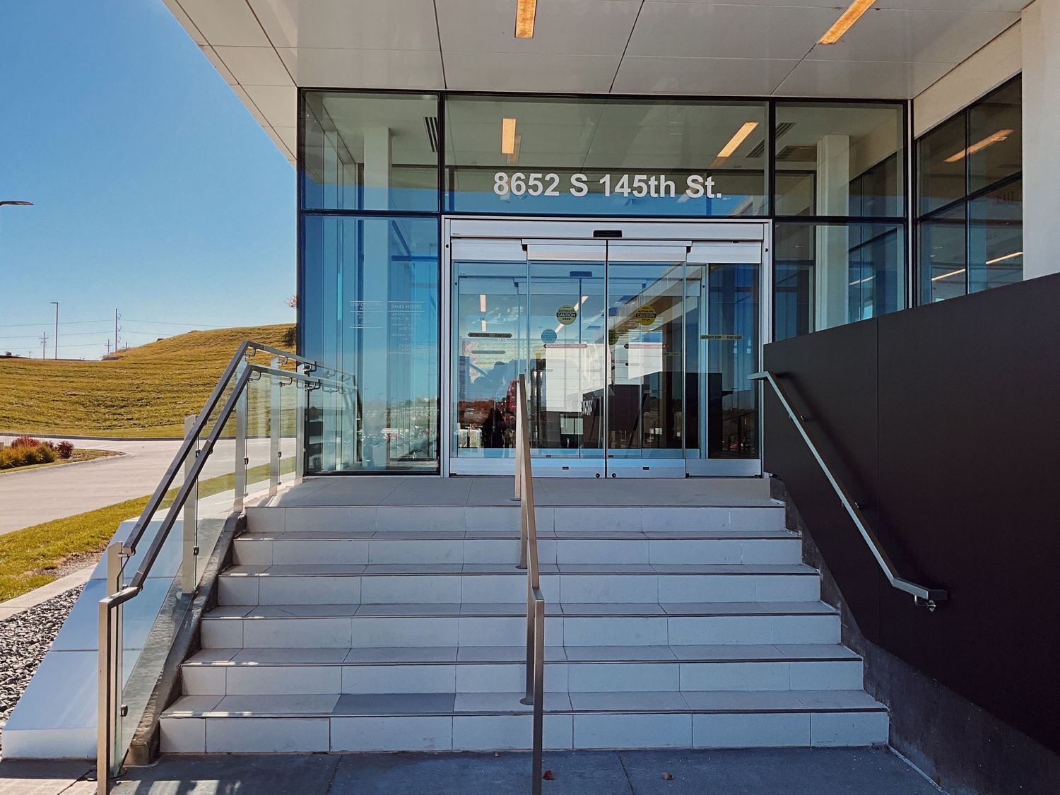 Modern glass entrance of 8652 S 145th St office building with steps, railings, and green hillside backdrop.