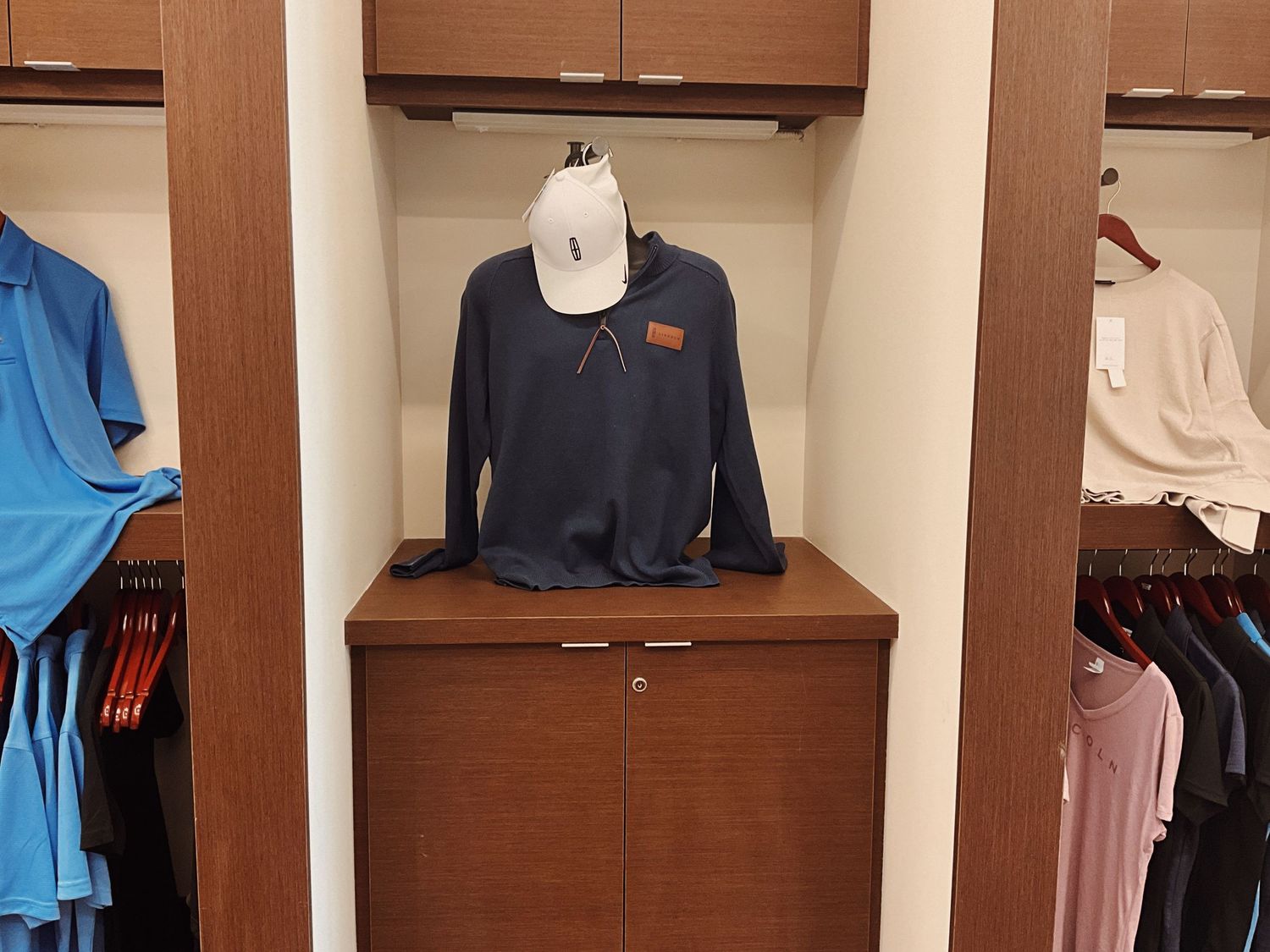 Navy blue quarter-zip pullover displayed on a mannequin head atop a wooden cabinet in a retail clothing store.