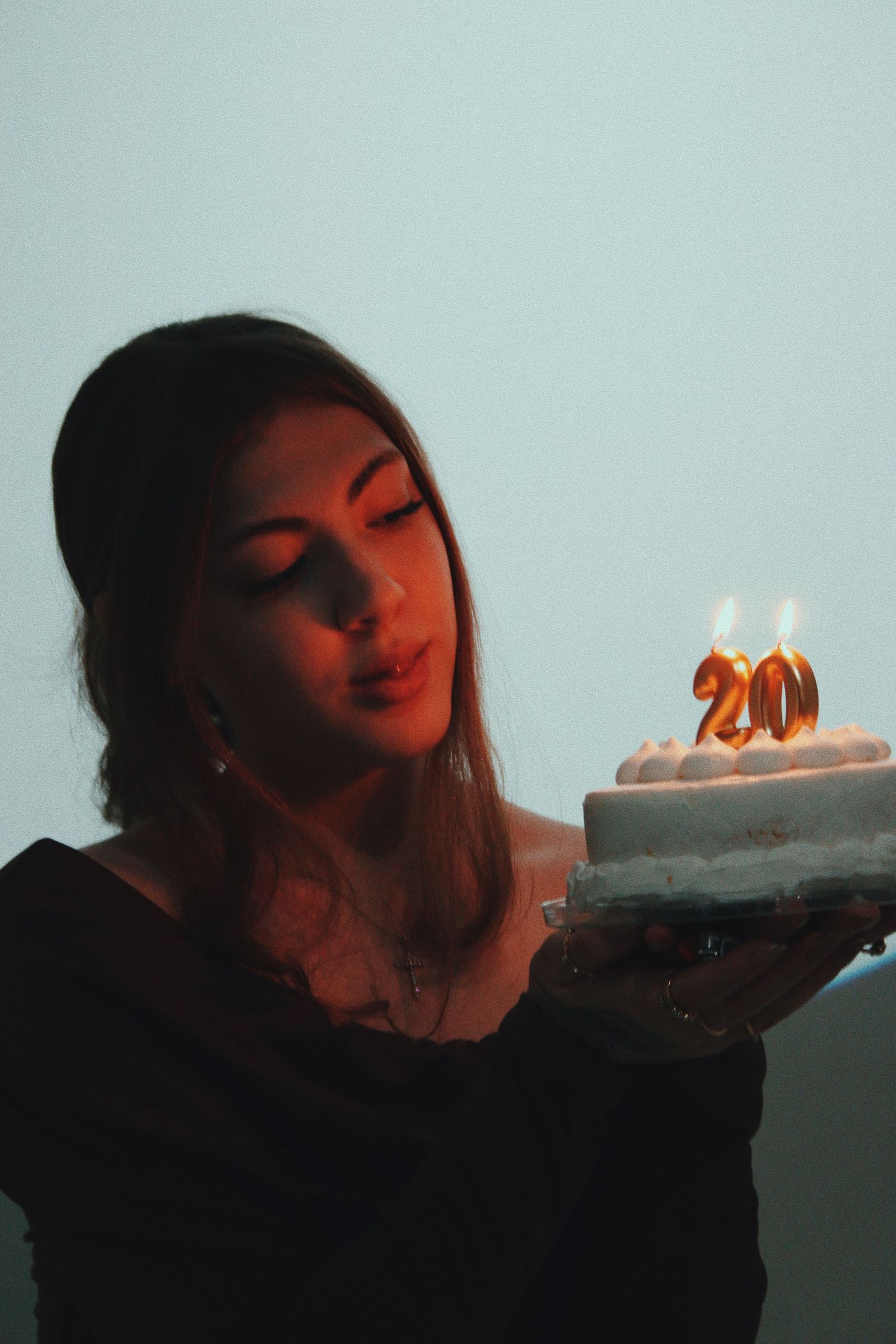 Young woman blowing out candles on a 20th birthday cake in warm candlelight.