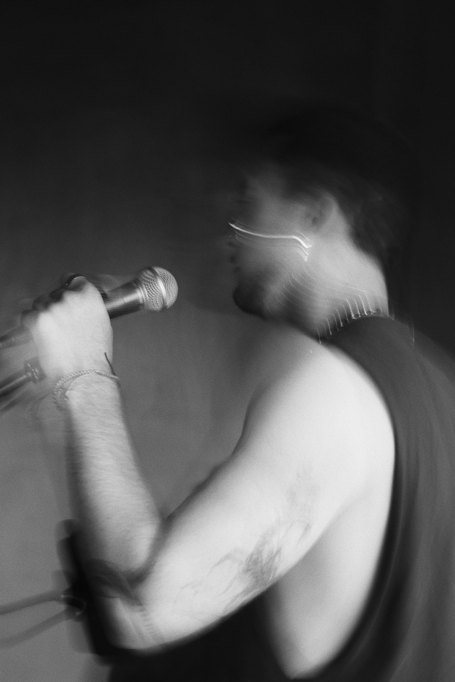 Black and white motion blur photo of shirtless male singer performing with microphone at live concert.