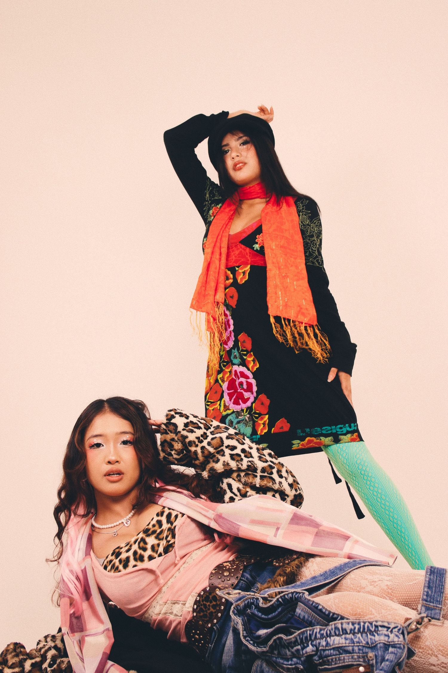 Two stylish Asian women posing in colorful eclectic outfits, one wearing an orange scarf and floral dress.